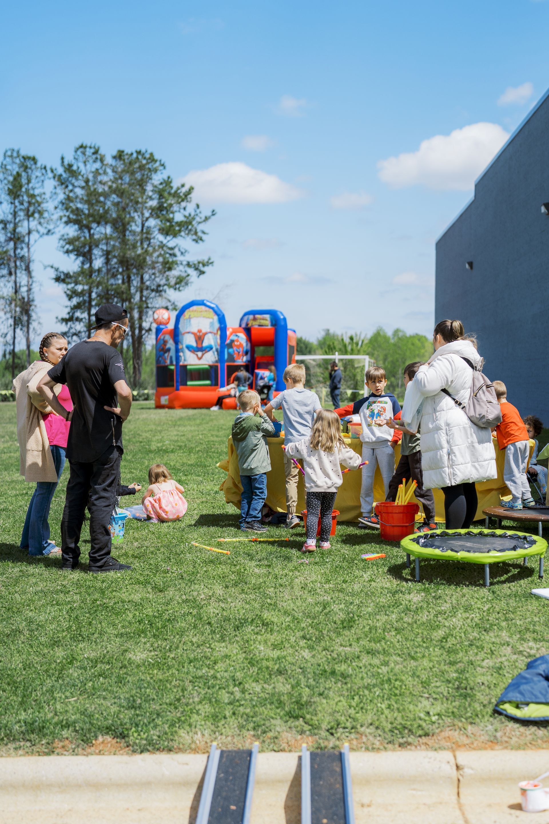 Children and adults gathered on a sunny lawn near playground equipment beside a building