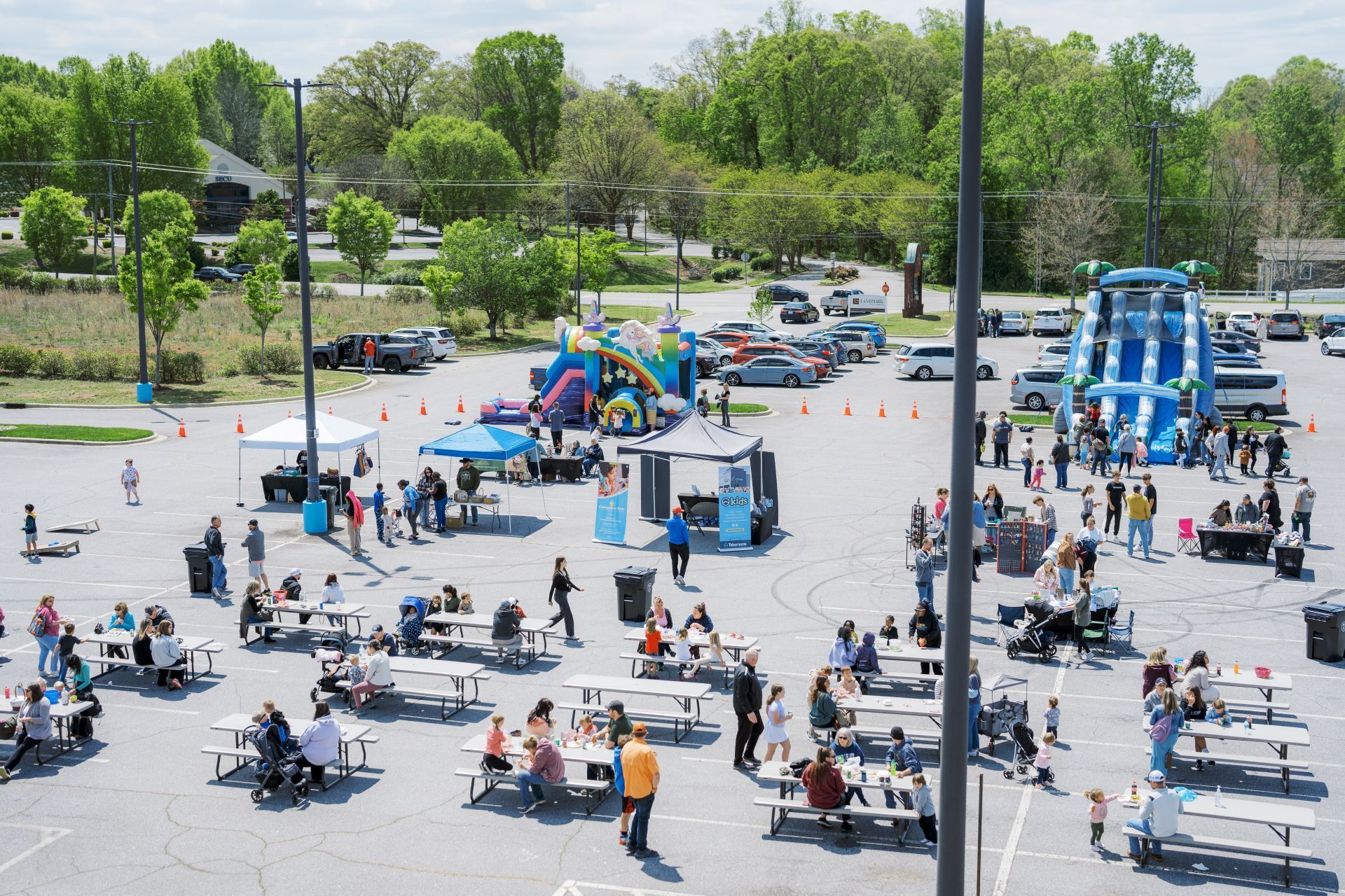 Crowded outdoor plaza with people seated at tables, children playing, and colorful playground equipment nearby