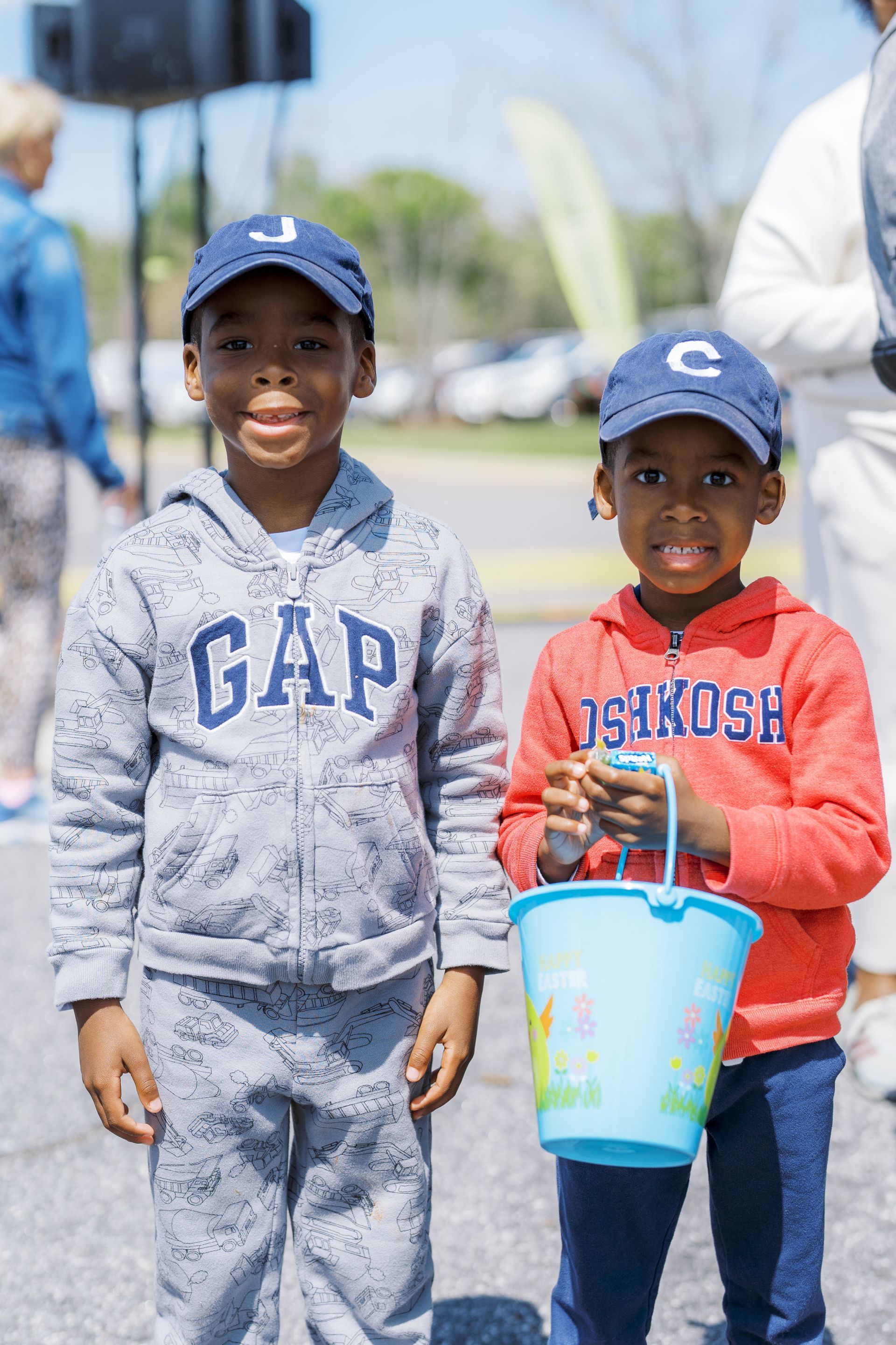 Two children in GAP hoodies holding a blue bucket outdoors on a sunny day