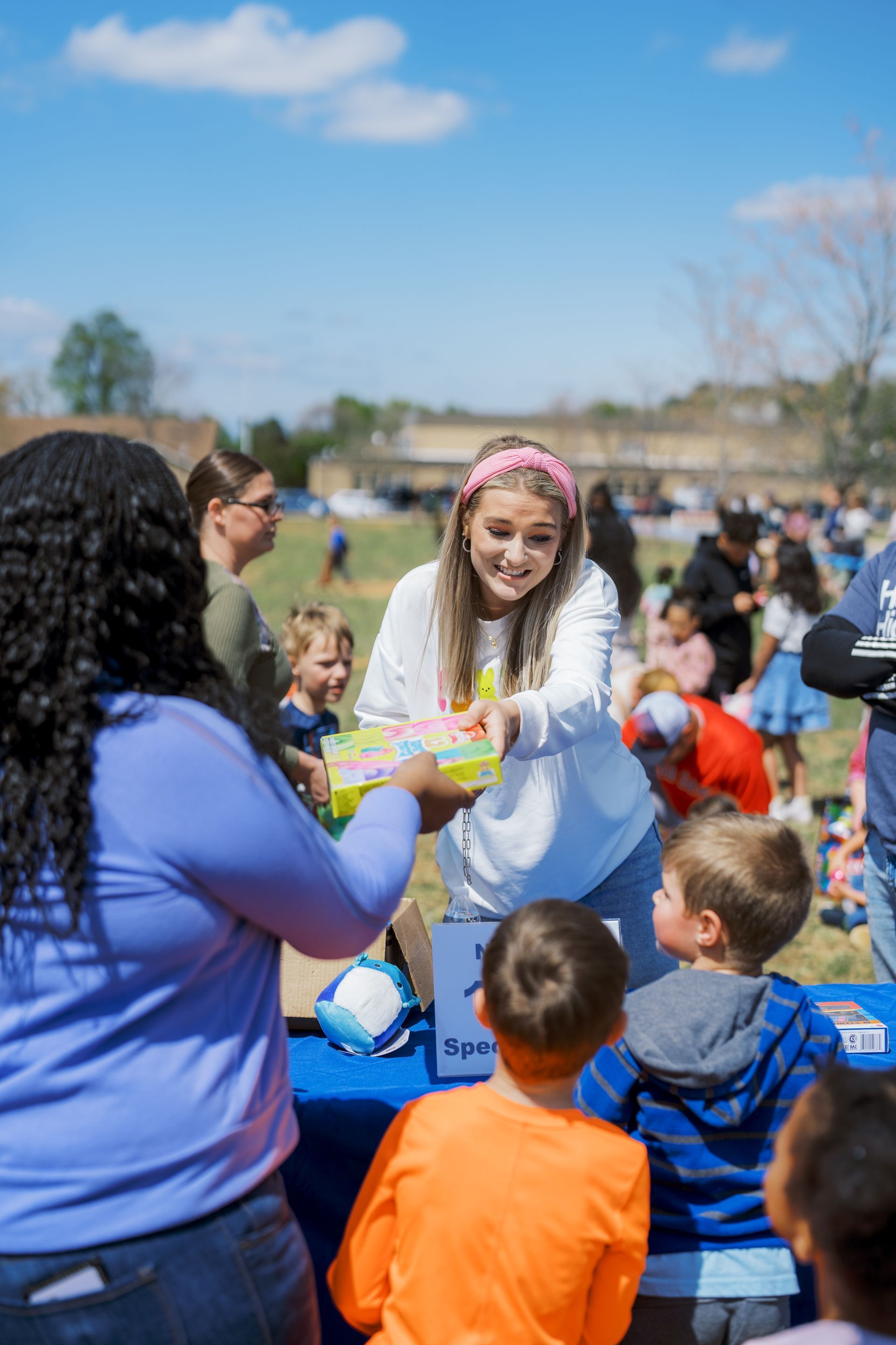 Volunteer handing out items to children outdoors on a sunny day