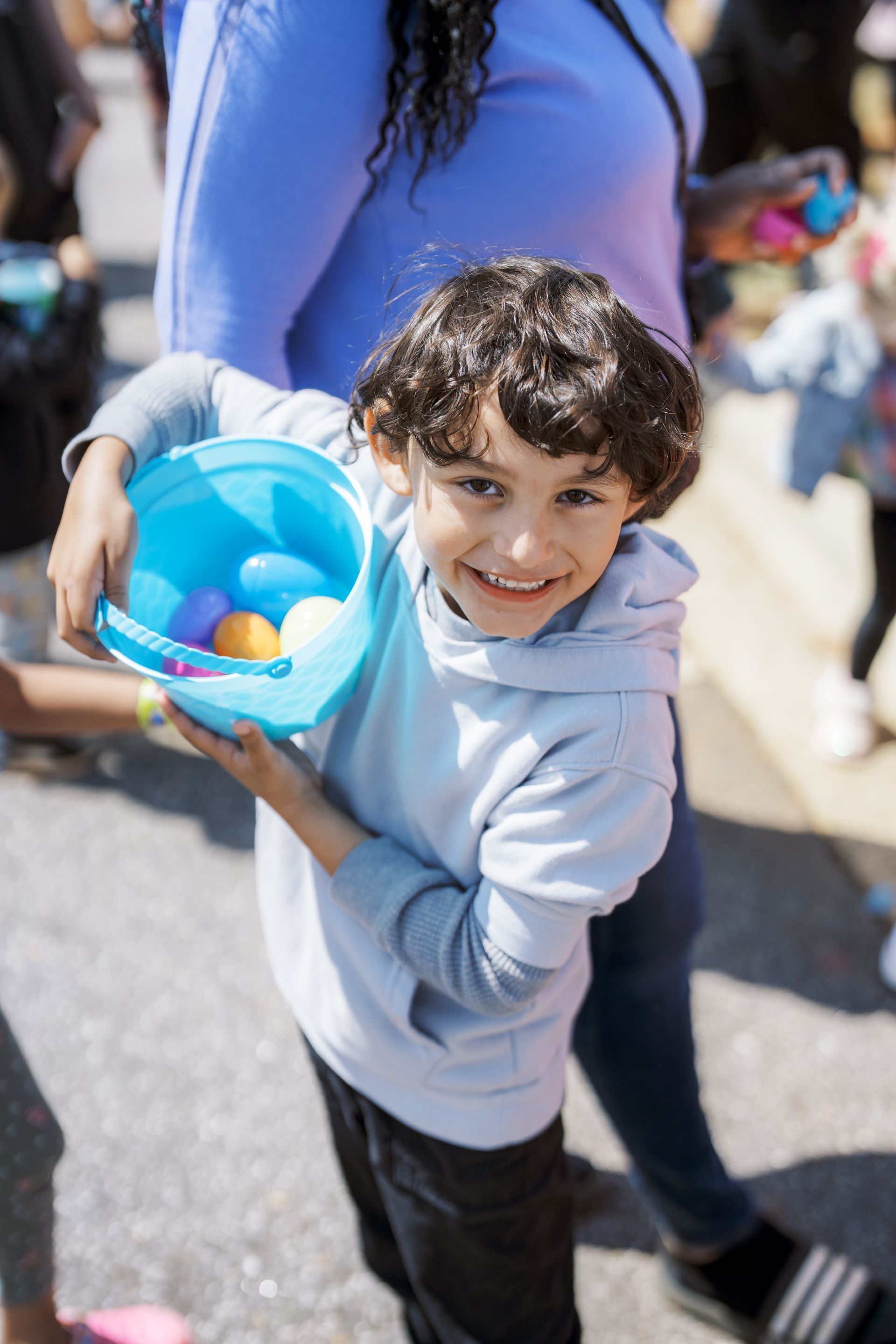 Child smiling and holding a blue bucket with colorful balls at an outdoor event