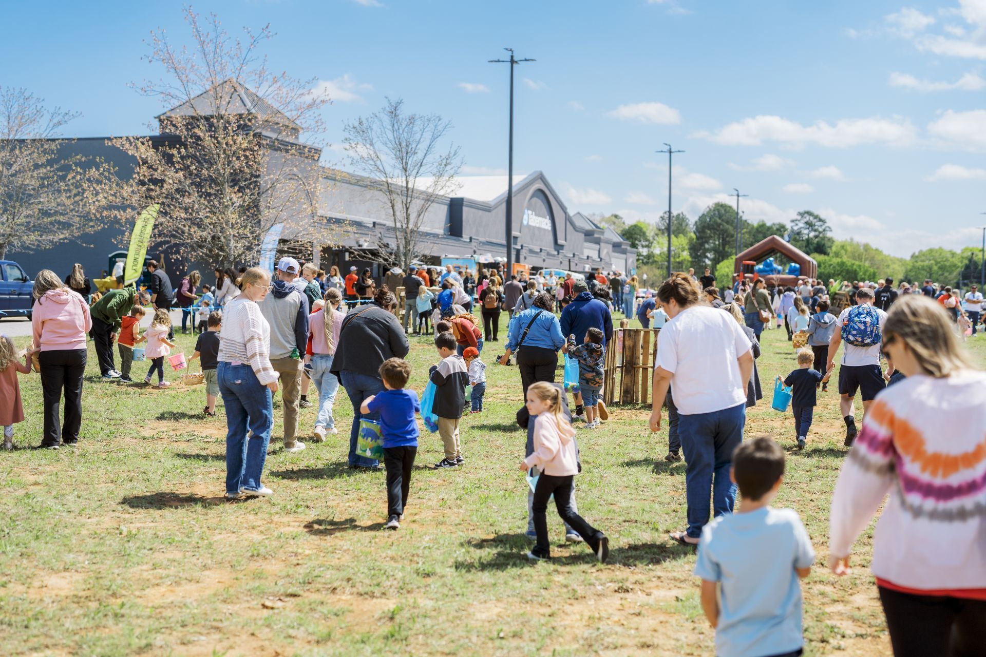 Crowd at an outdoor community event on a sunny day near a stone building and white tent