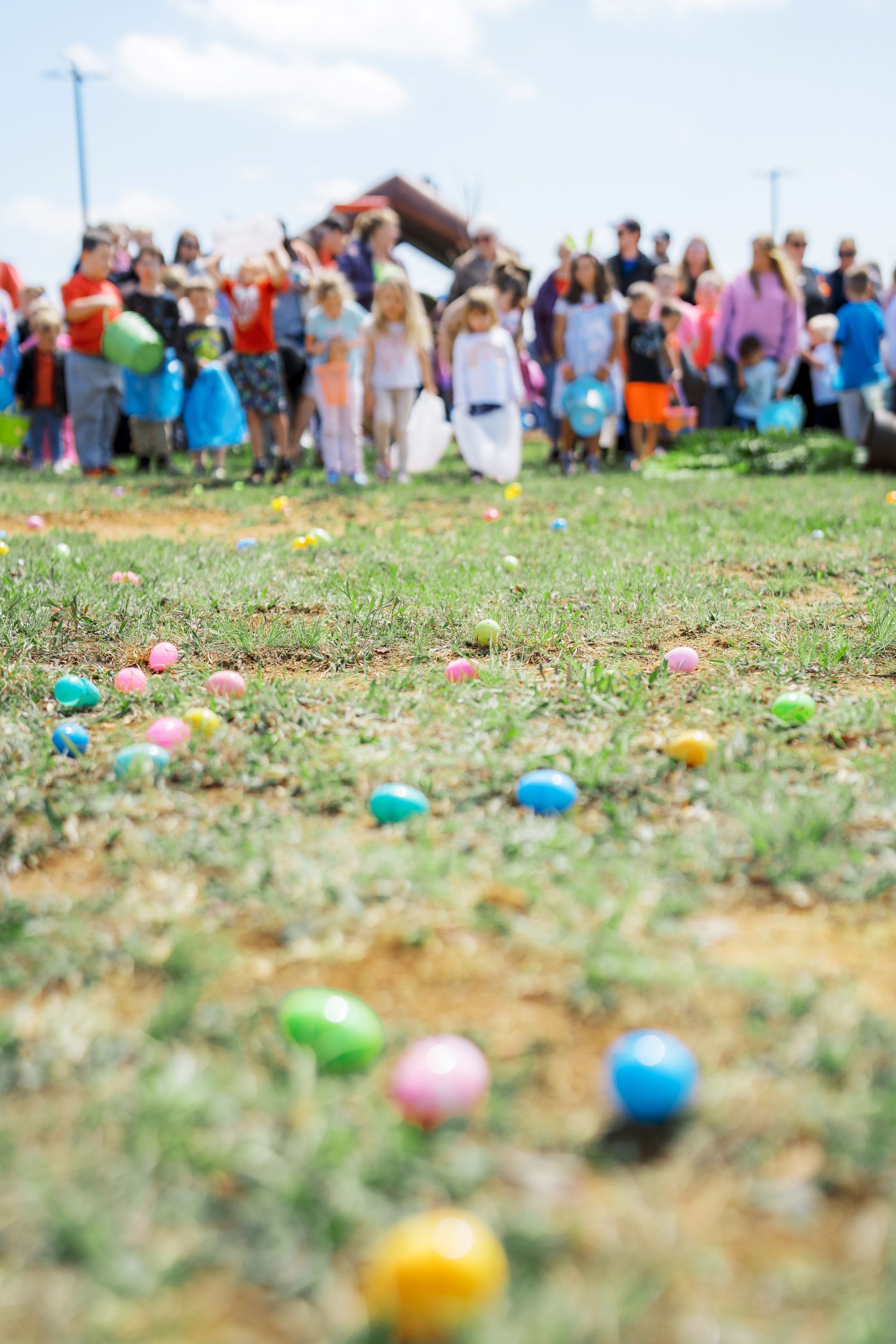 Colorful Easter eggs scattered on grass with a blurred crowd gathered in the background