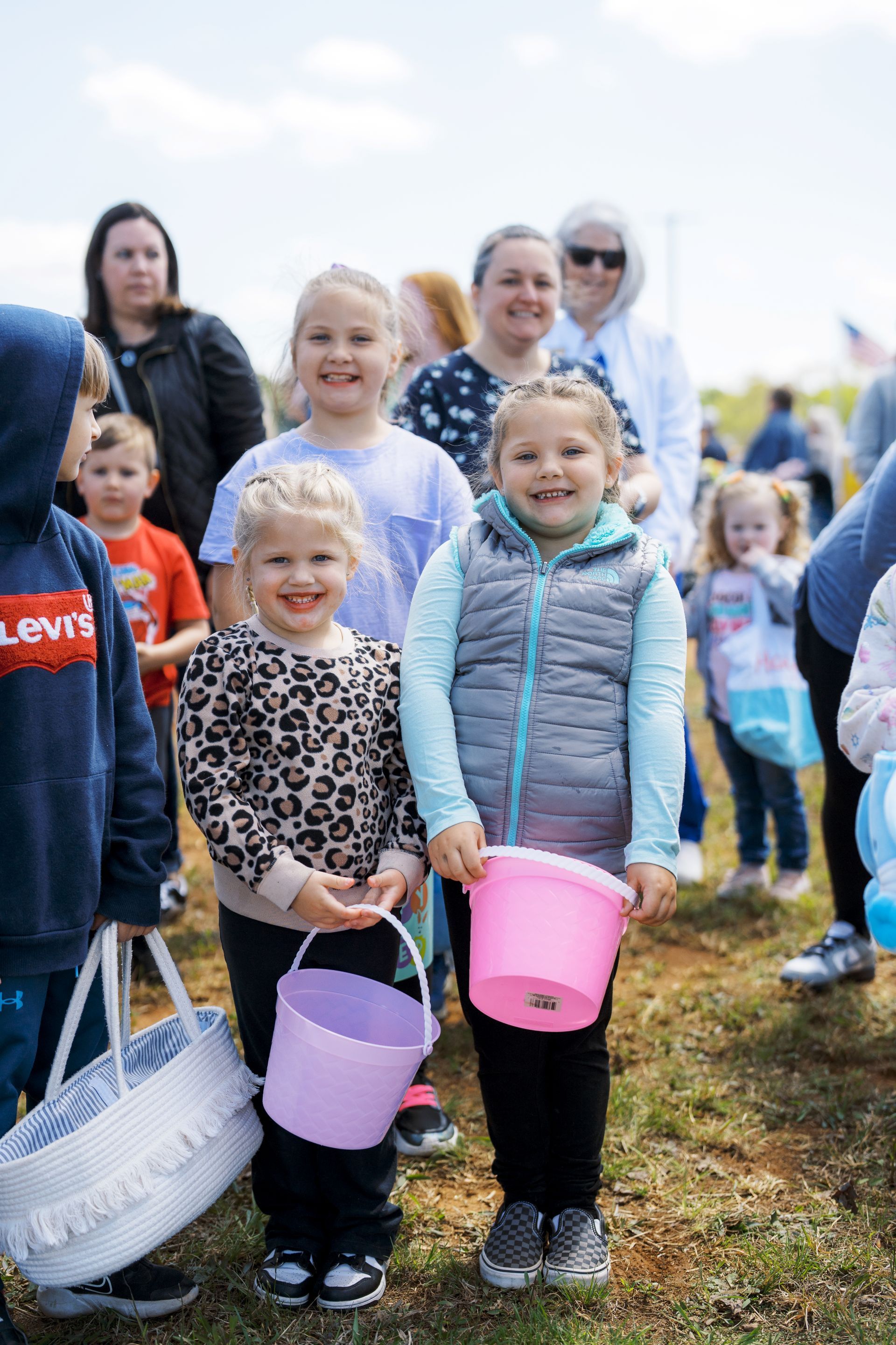 Children holding colorful buckets at an outdoor gathering on a grassy field