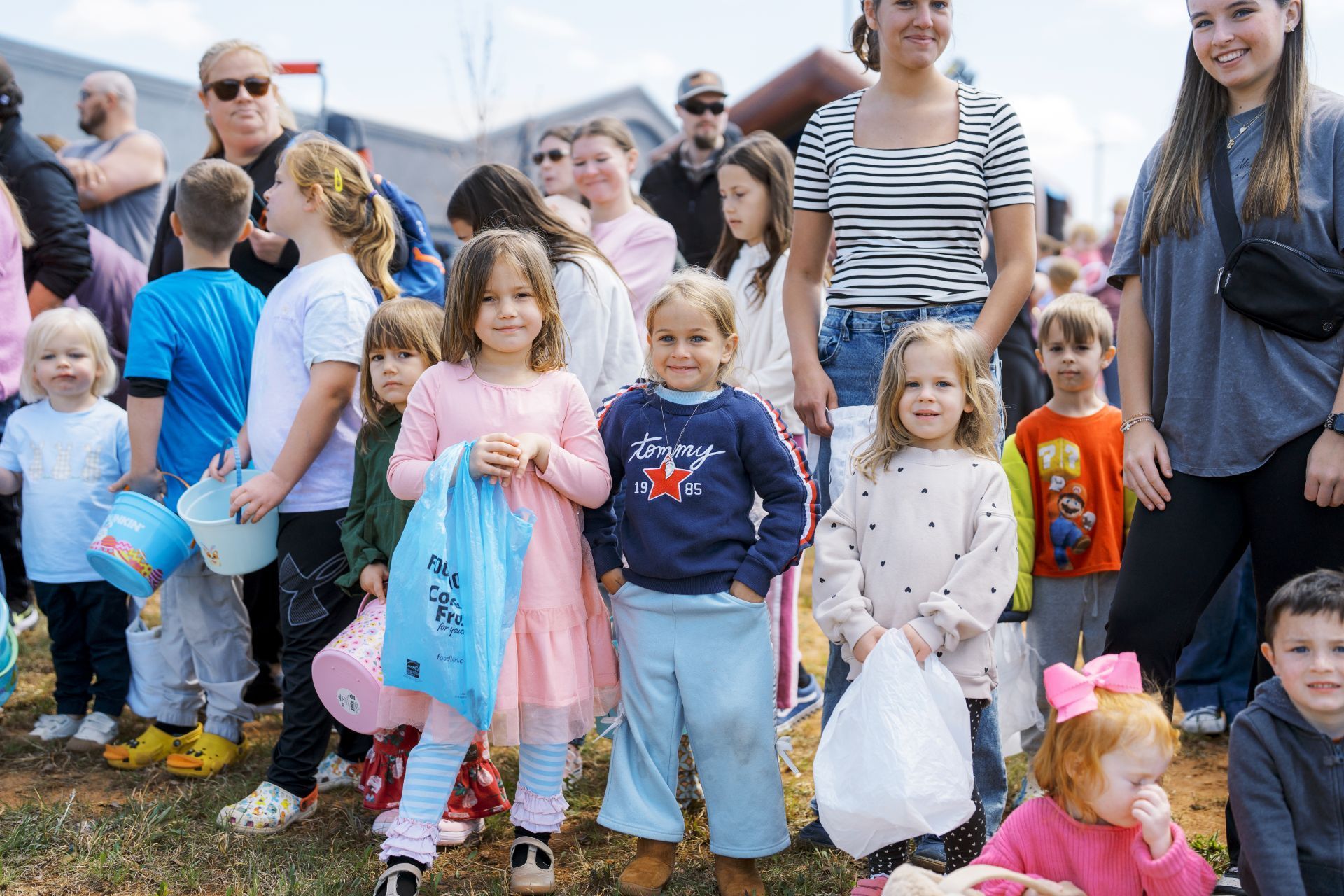 Children holding candy bags at an outdoor event with adults in the background