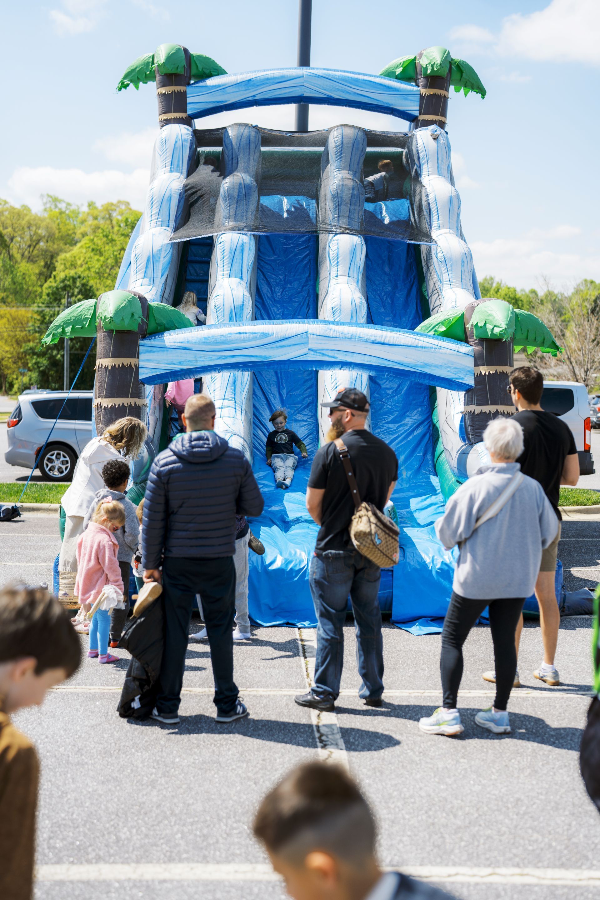 People standing around a blue inflatable water slide at an outdoor event on a sunny day