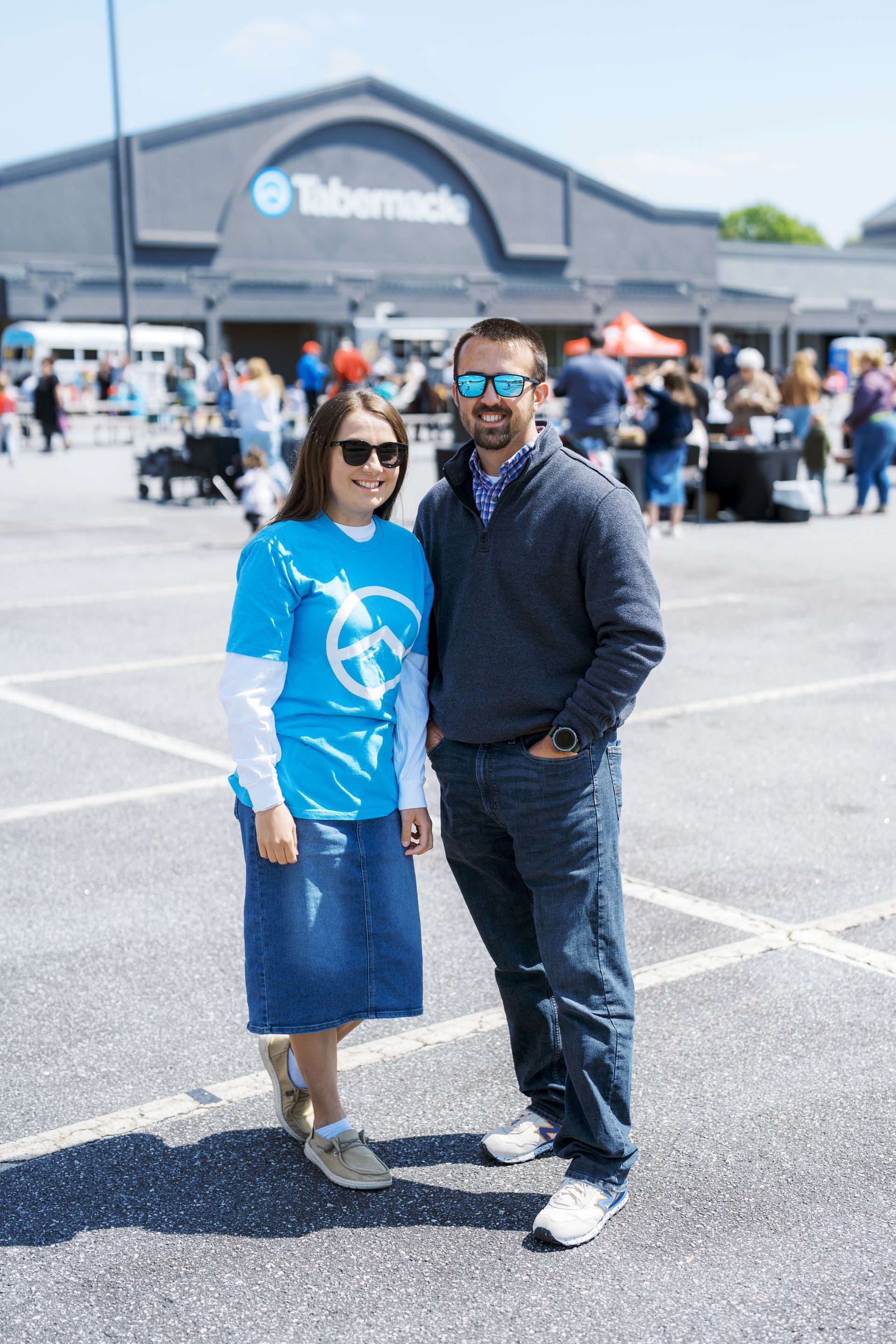 Two people posing outside a Telenor store, one in a blue shirt and skirt, the other in dark clothes and sunglasses.