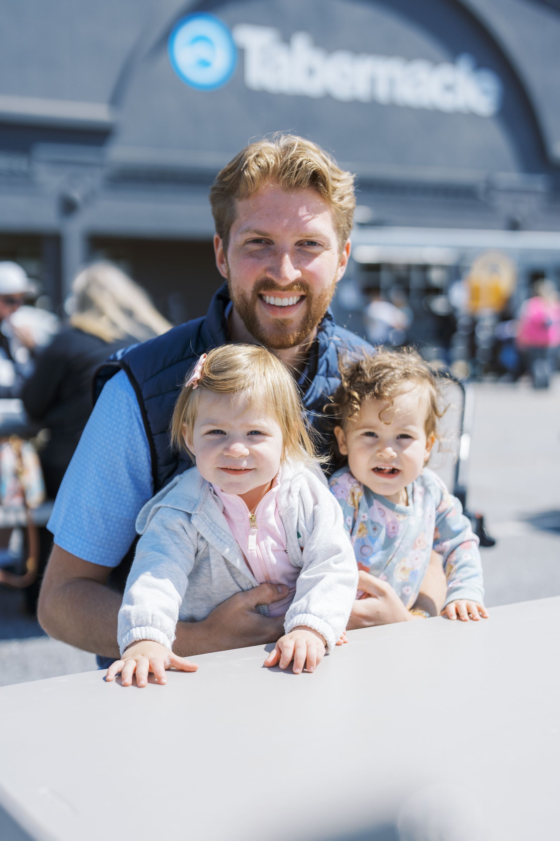 A smiling man with two small children in front of a Tiberdeck building outdoors