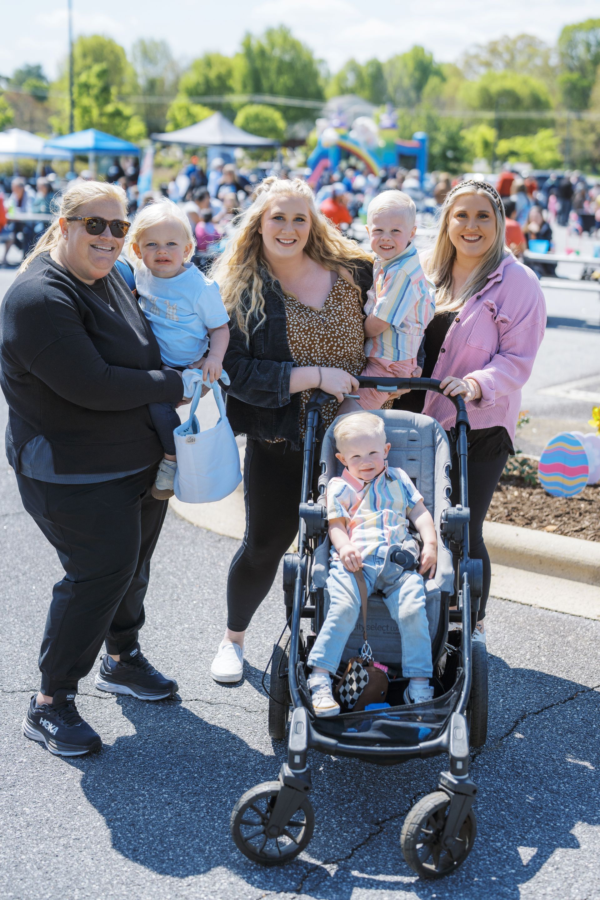 Four people posing outdoors at a community event, with a child in a stroller in front.