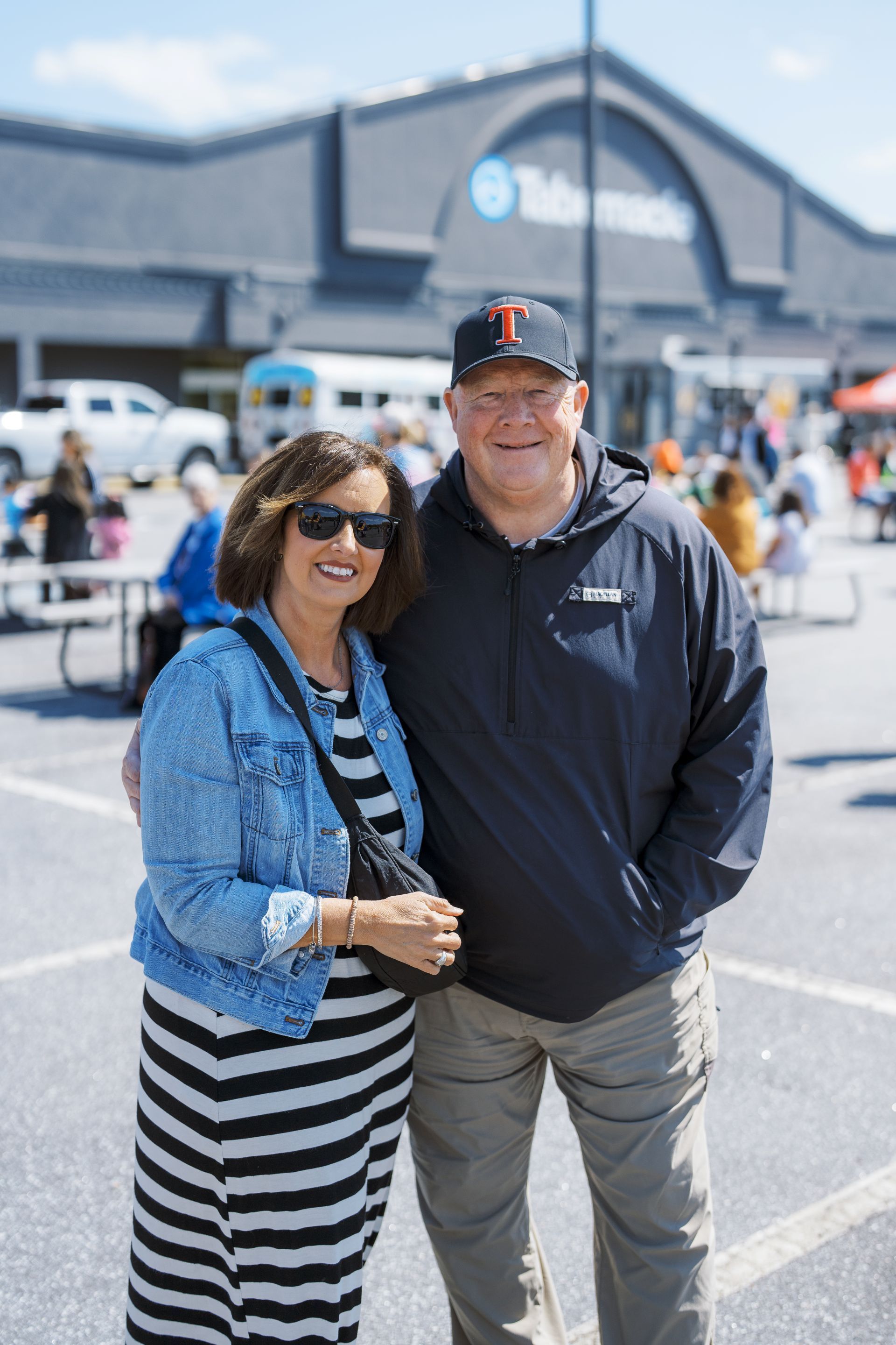 Two smiling people standing outside a large building on a sunny day