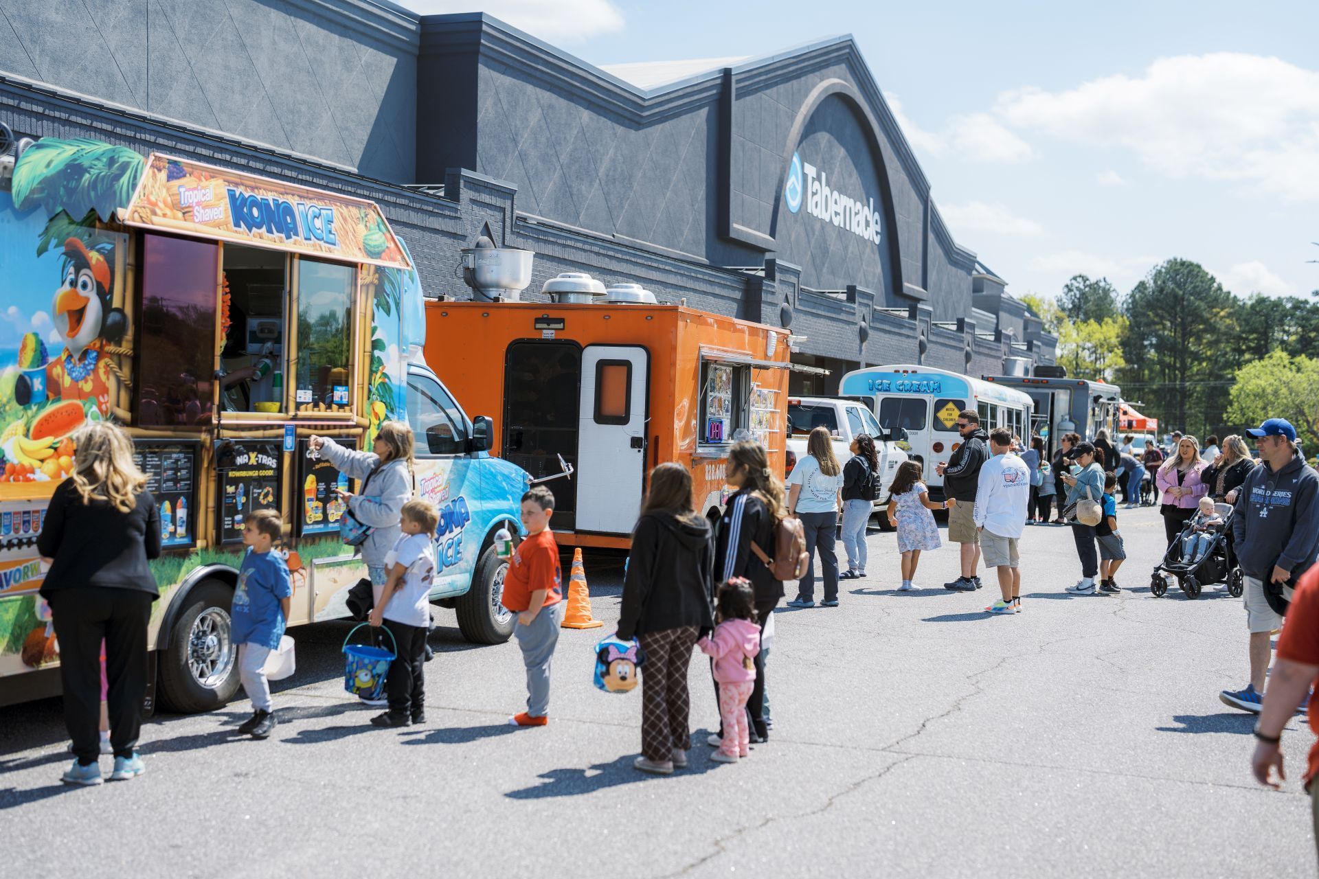 People lining up at colorful food trucks outside a market building on a sunny day