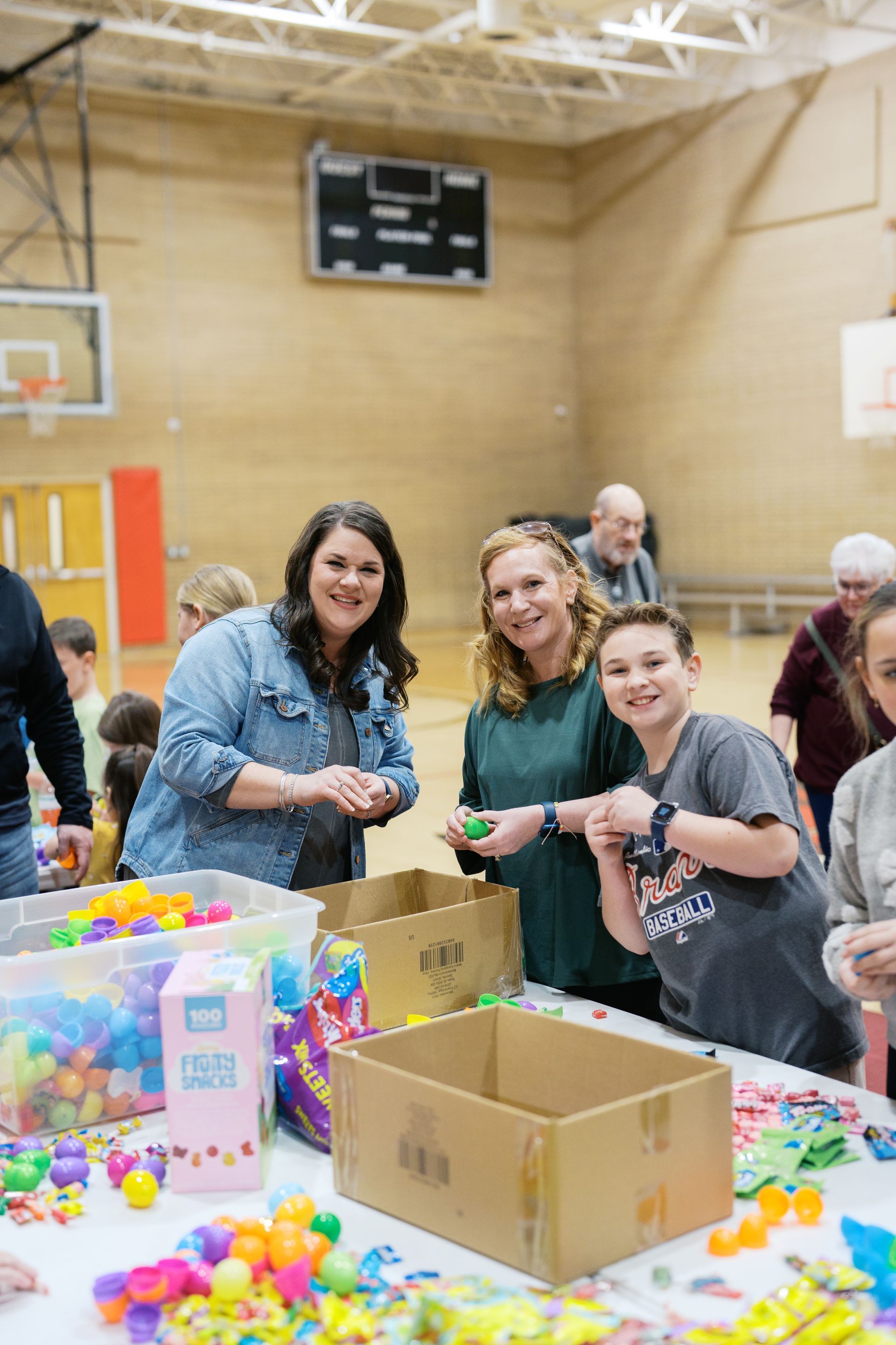 People packing colorful toys in boxes at a gymnasium table