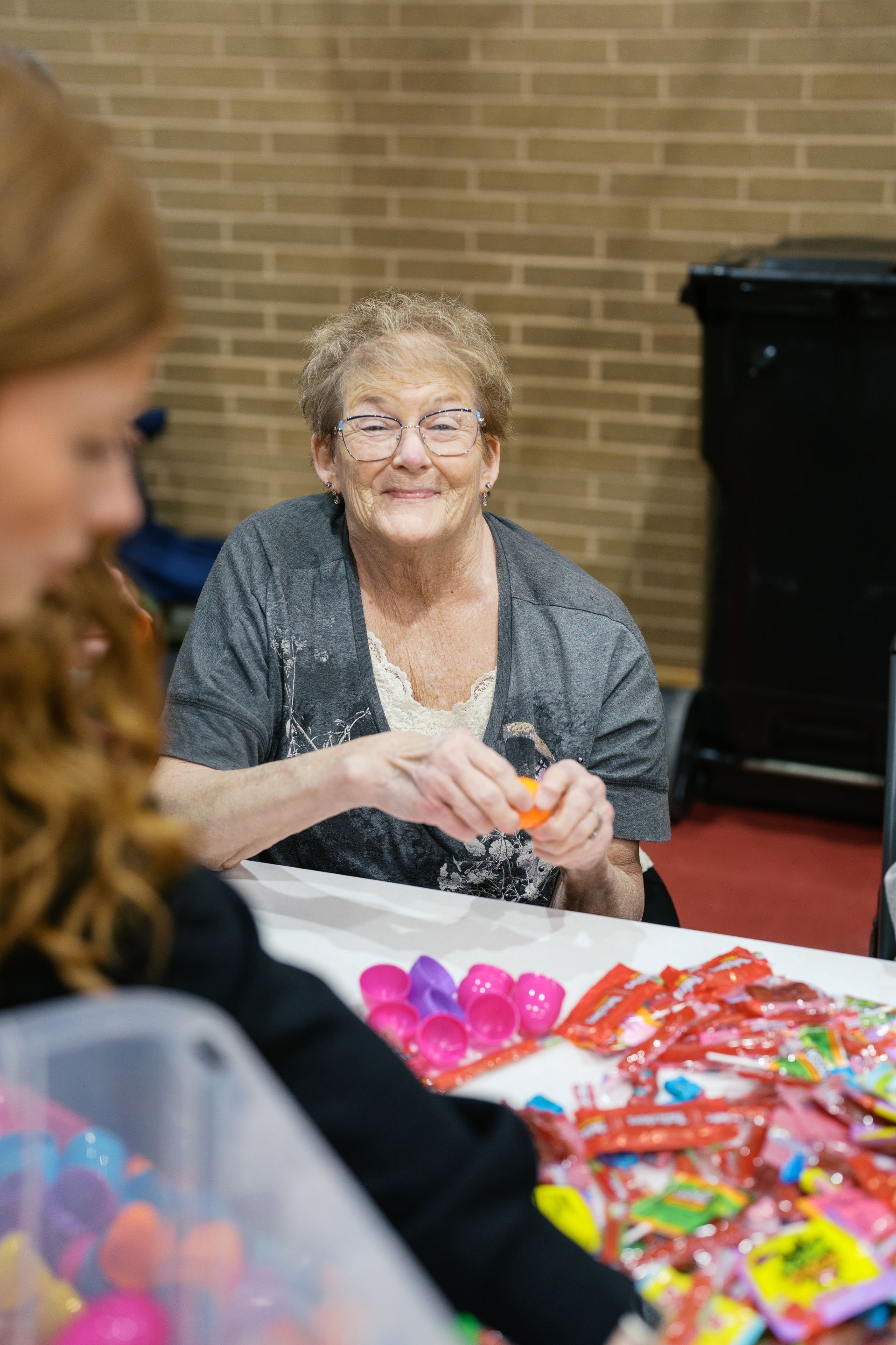 Woman smiling behind a table of colorful wrapped candies at an indoor event