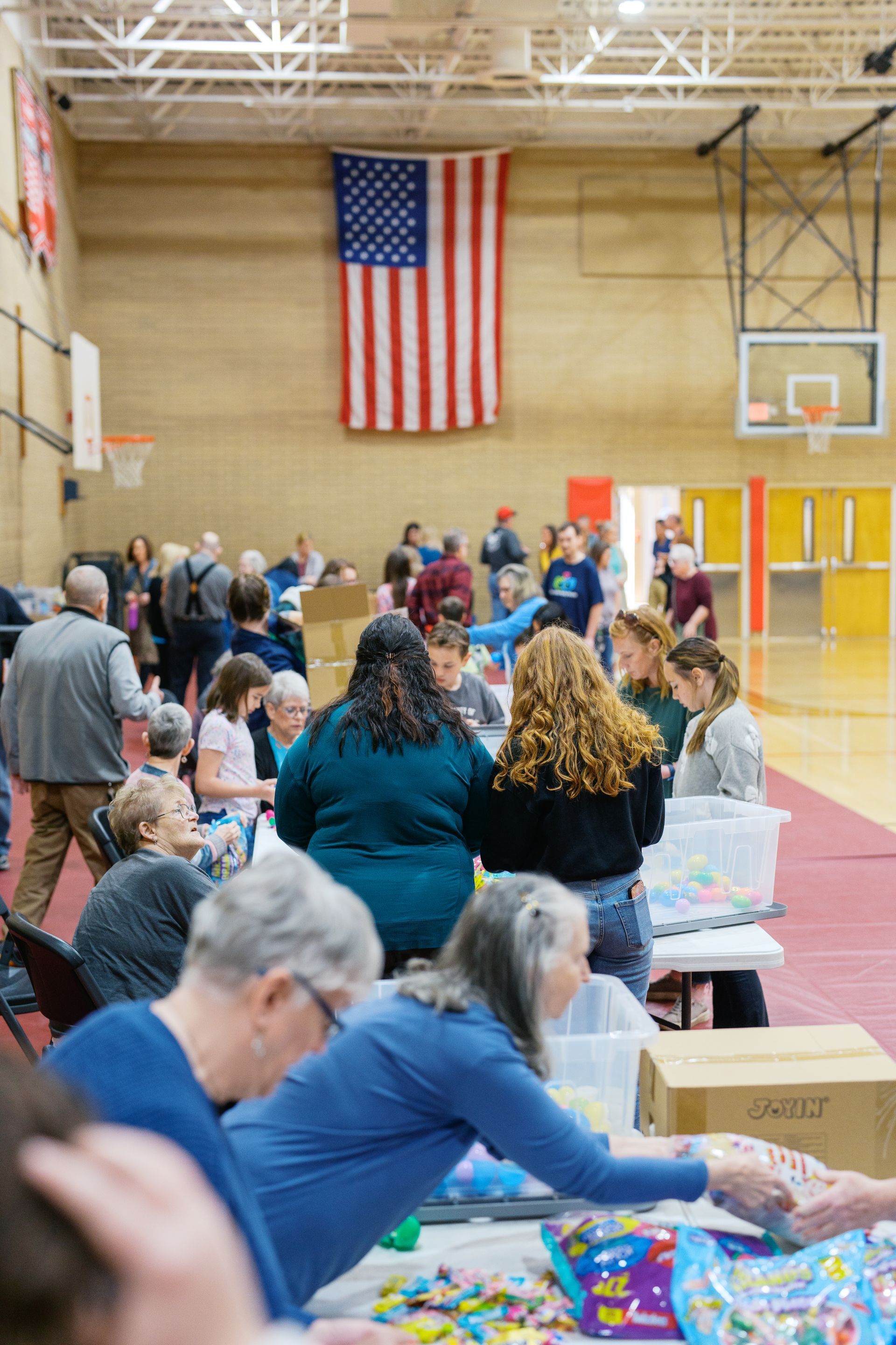 Community gymnasium with people at tables and an American flag hanging on the wall.