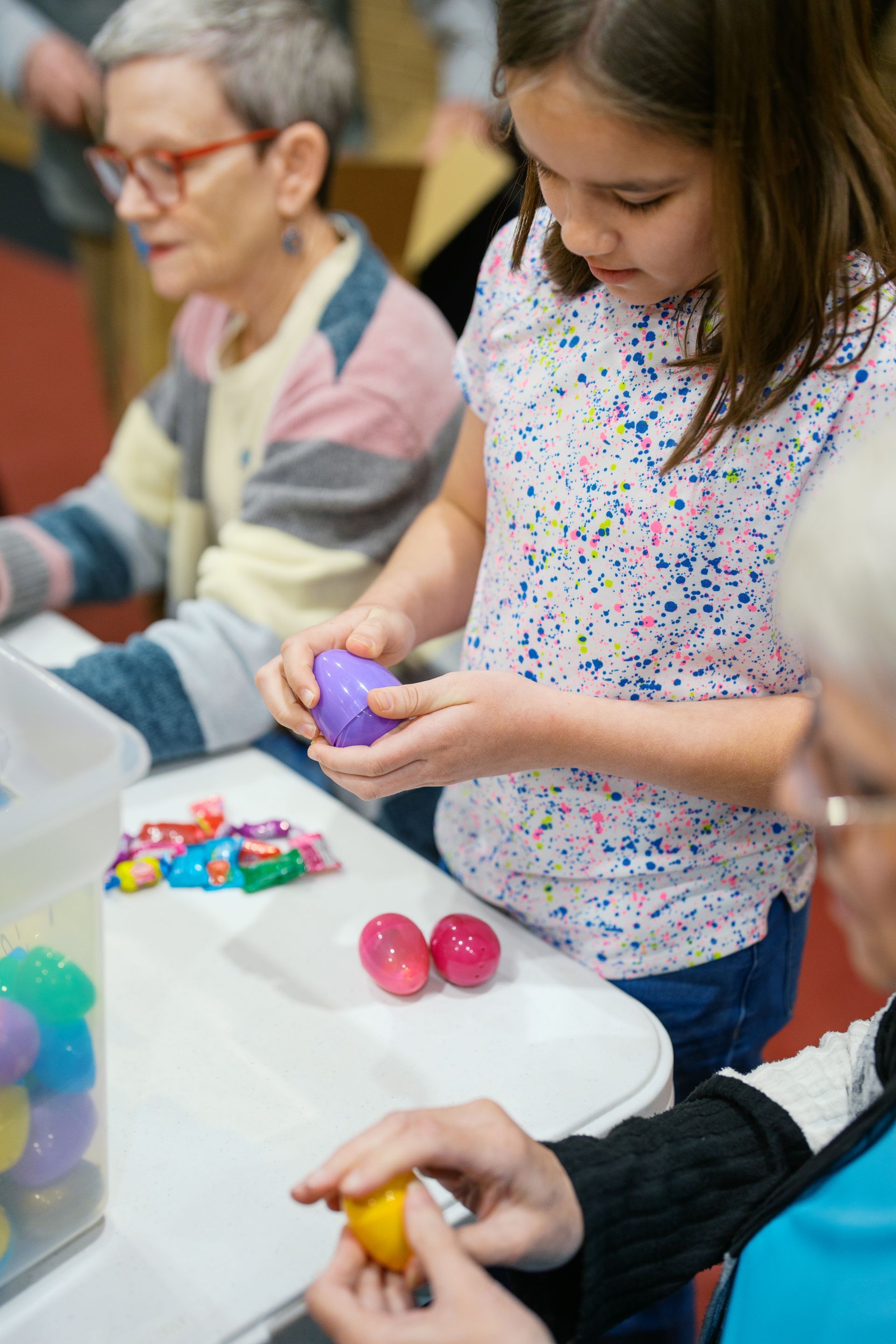 People handling colorful plastic eggs and small toys at a table during a craft activity