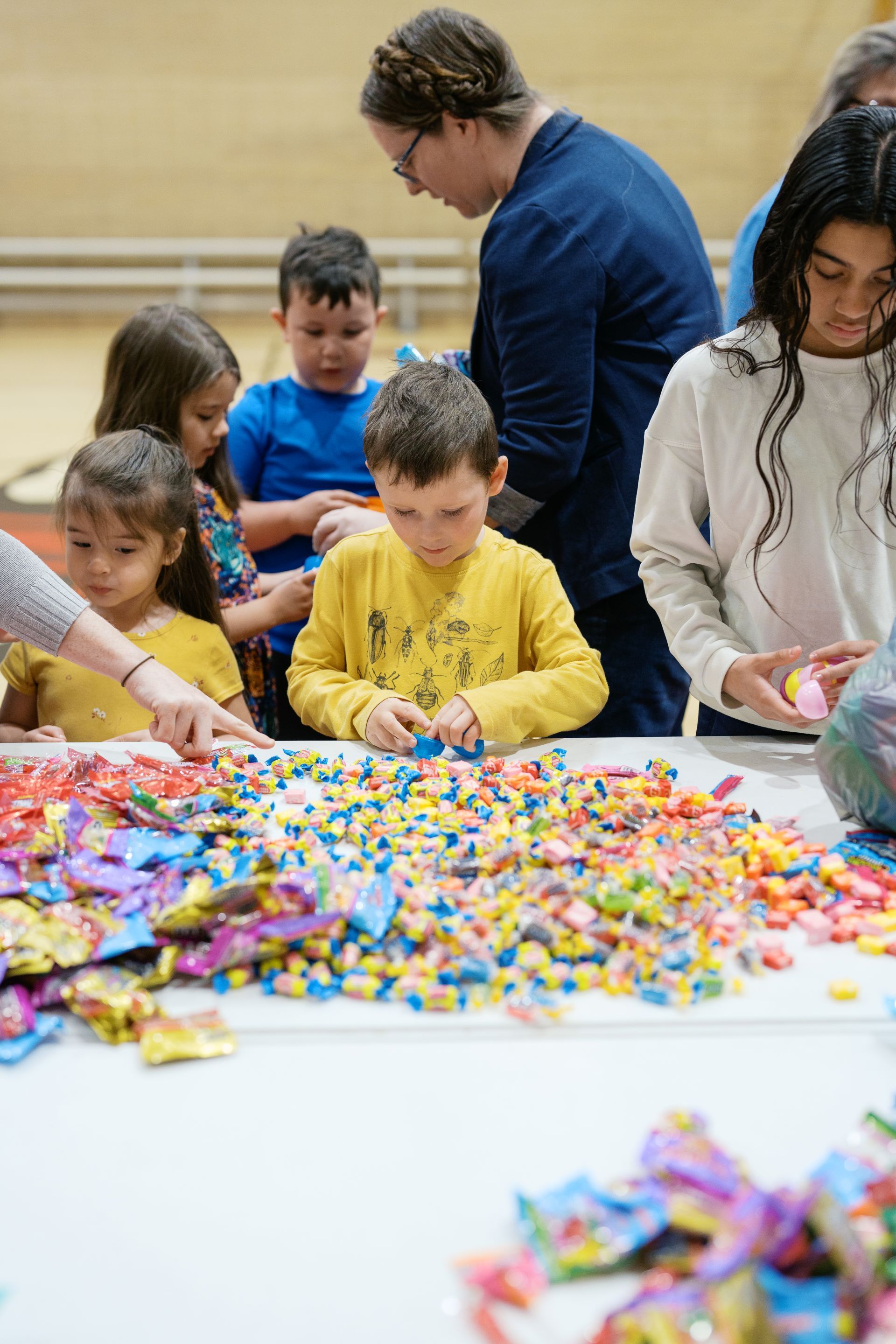 Children and adults sorting colorful candy on a table at an indoor event
