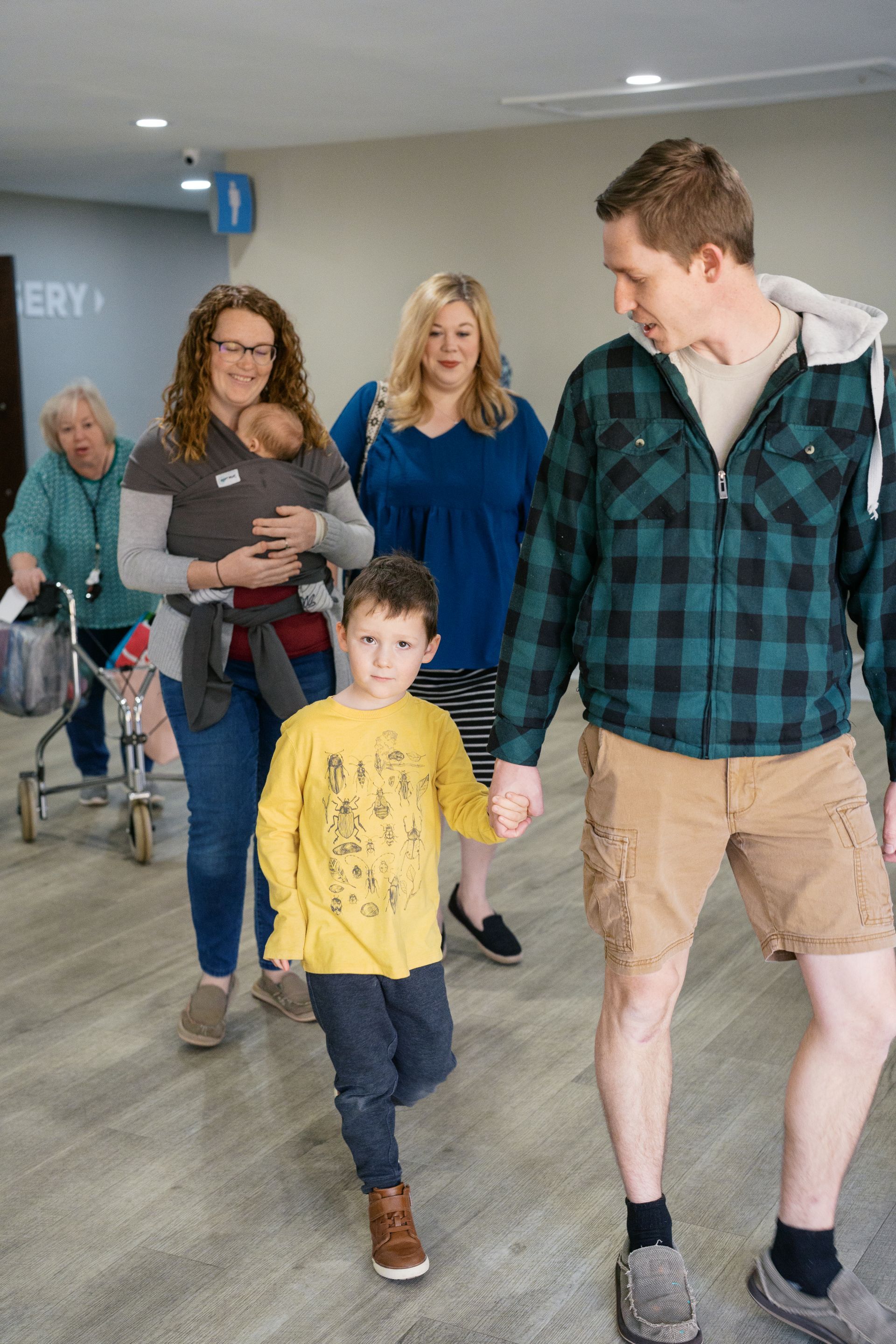 Family walking through a hospital hallway, with a man and young boy in front and women behind.