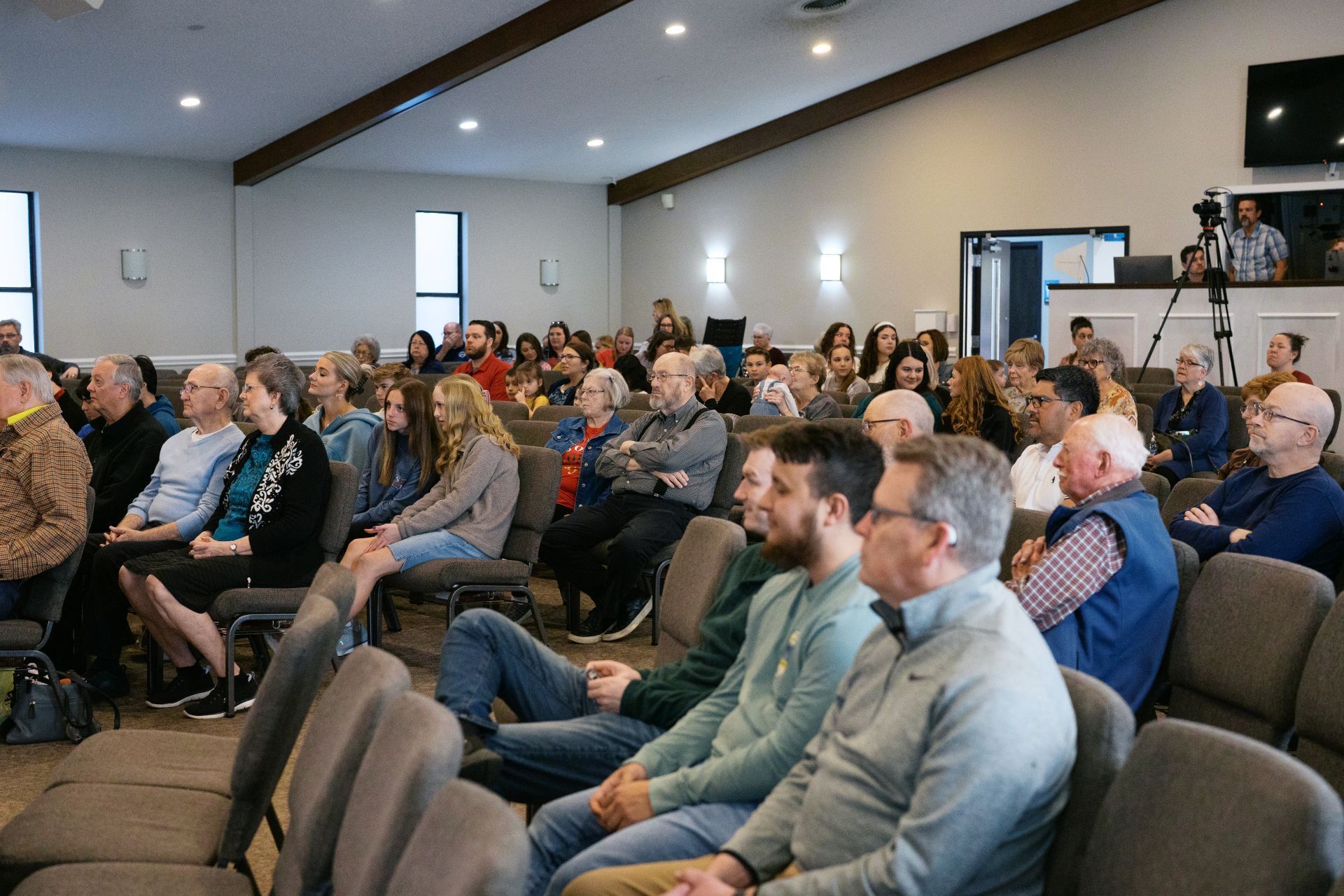 Audience seated in a meeting room, listening to a presentation near the front.