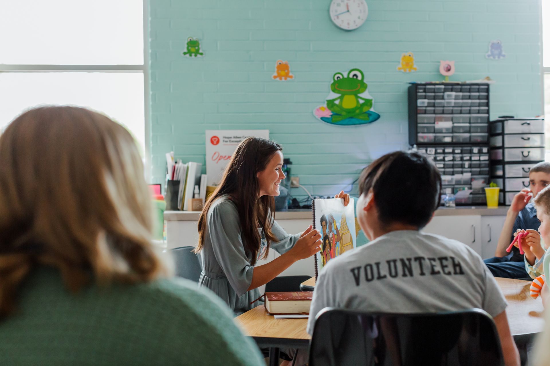 Volunteer meeting in a classroom, with a speaker at the front and seated attendees facing a frog mural.