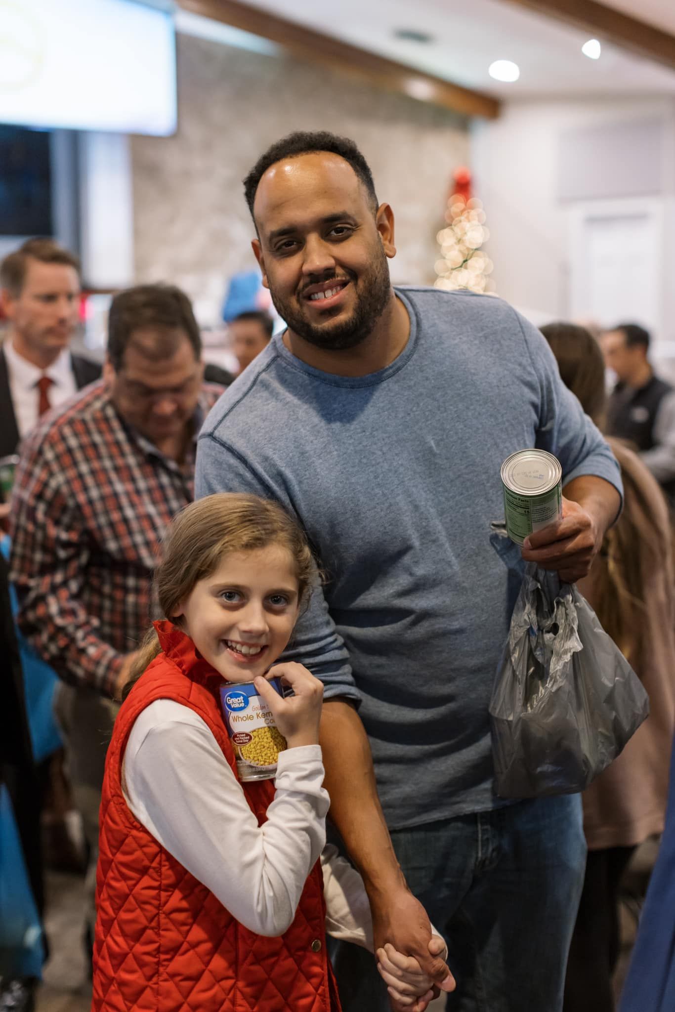 Man holding a small plant beside a smiling child in a red vest at an indoor event