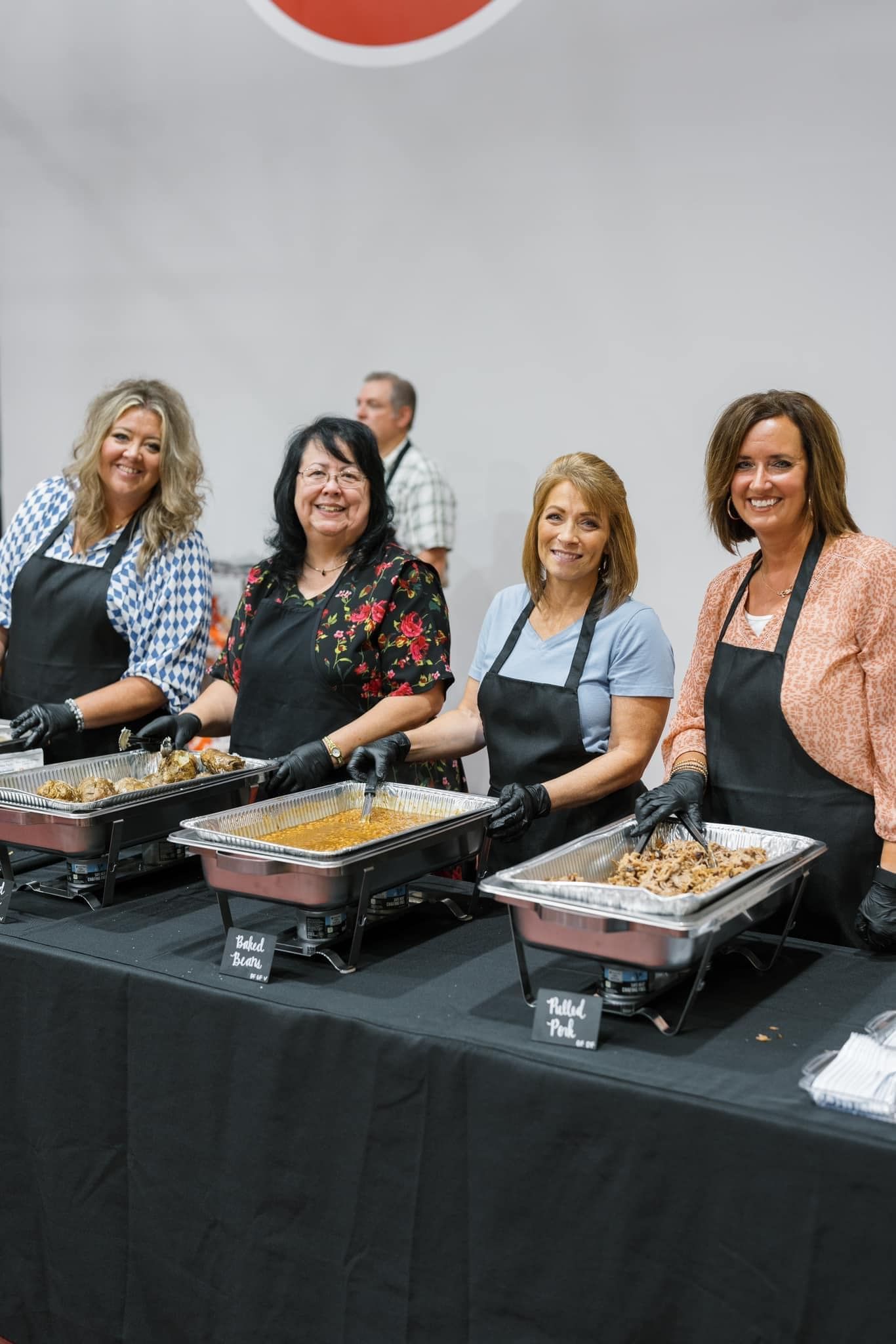 Four people serving food behind a black buffet table at an indoor event