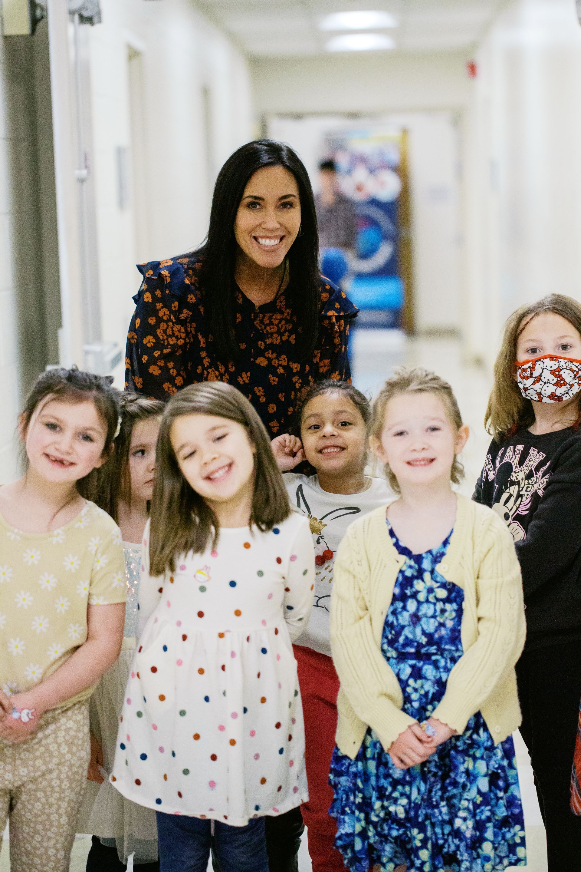 Teacher standing with five children in a school hallway, all smiling at the camera.