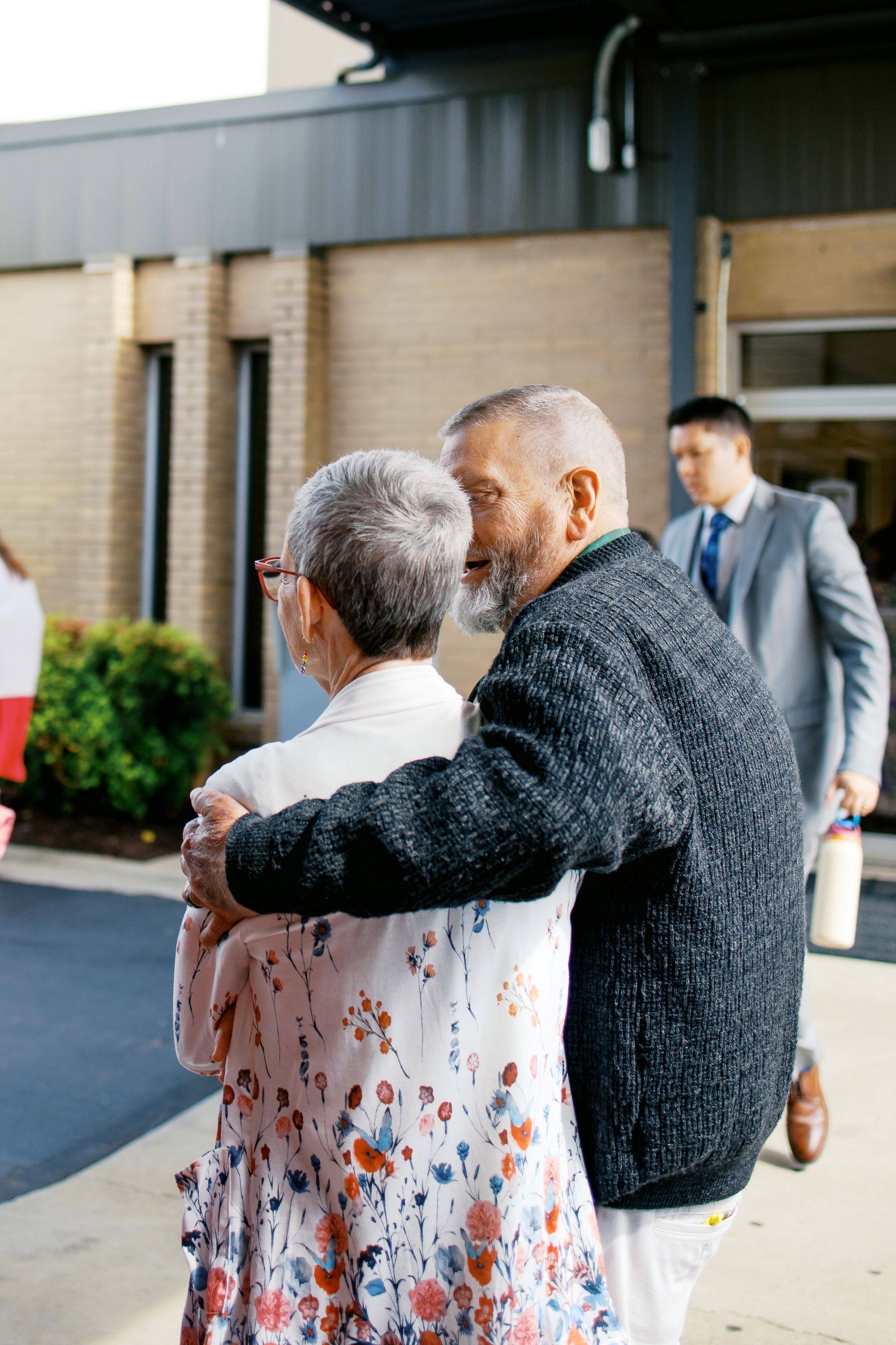 Two people embracing outside a building, with other attendees in the background