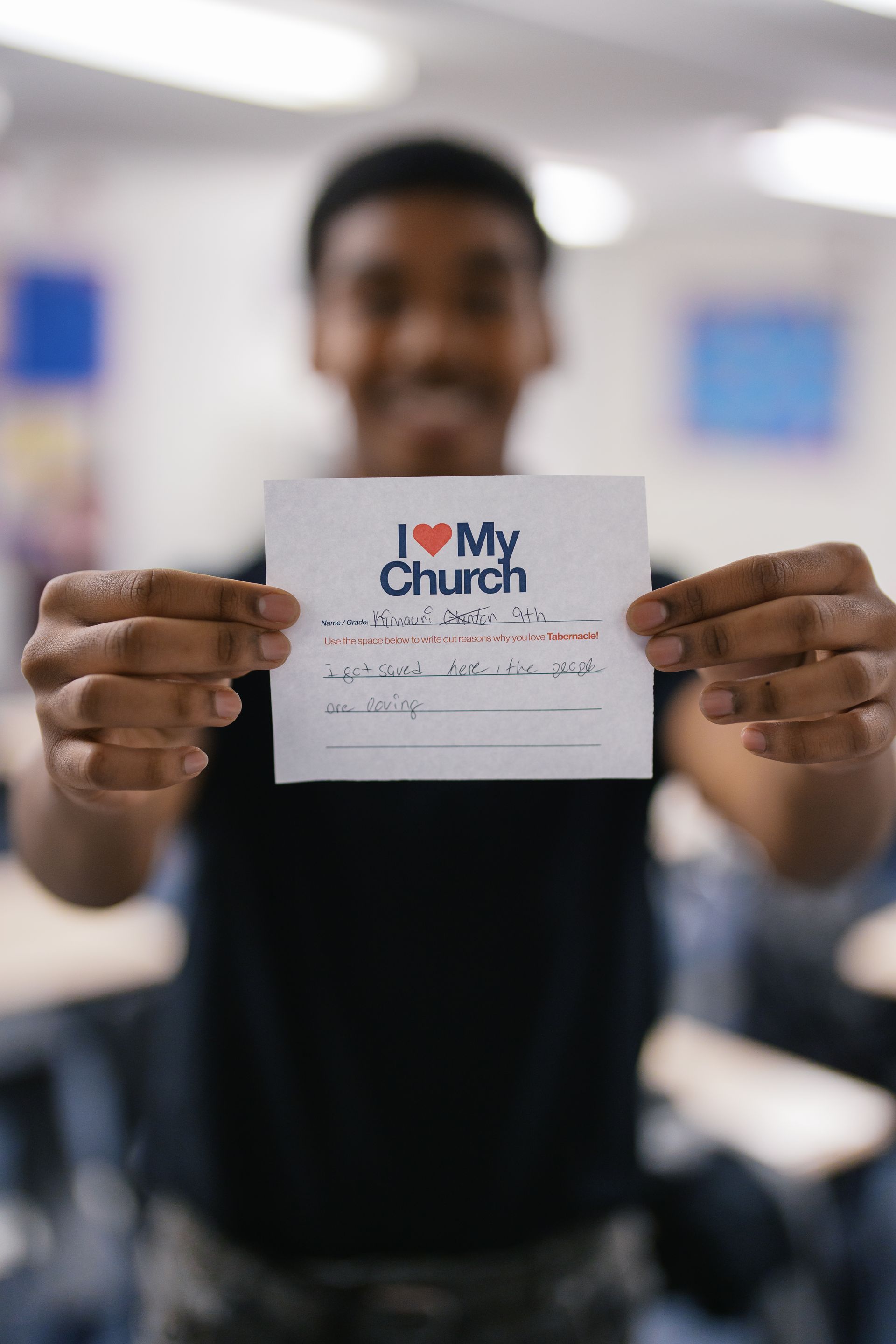 Person holding a card that says “I love my church” in a blurred indoor setting