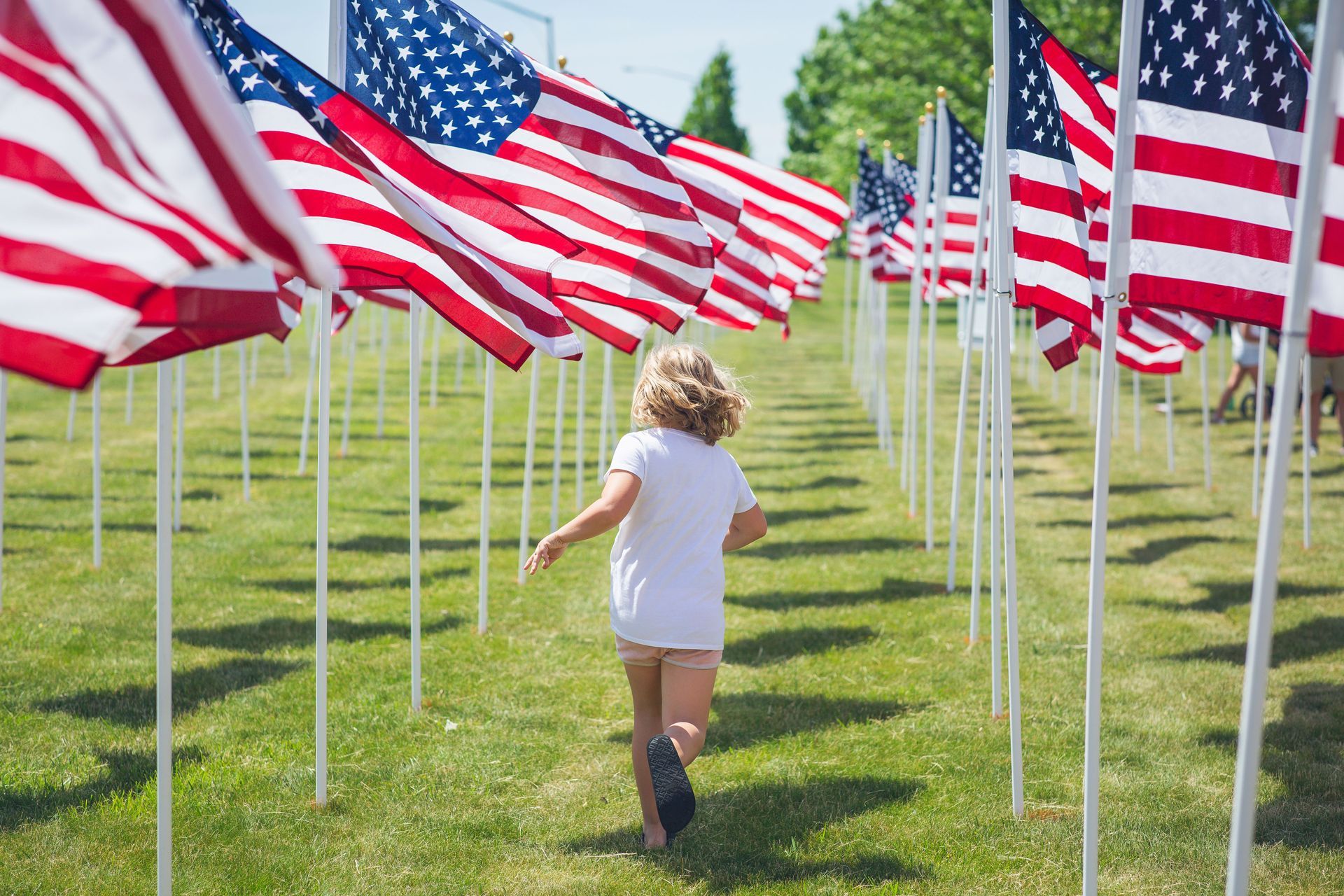 Child running between rows of American flags on a sunny green lawn