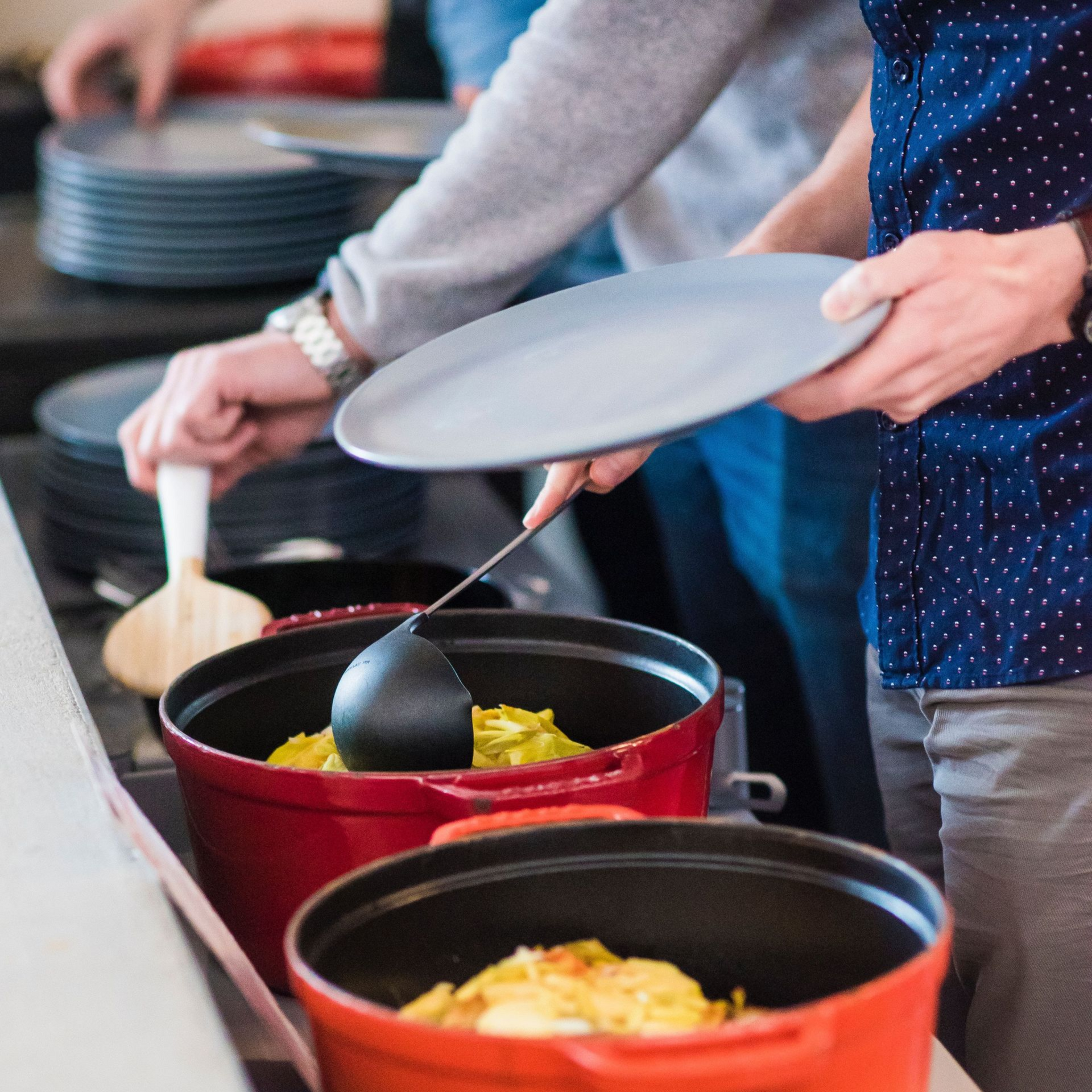 People serving food into red pots at a buffet table