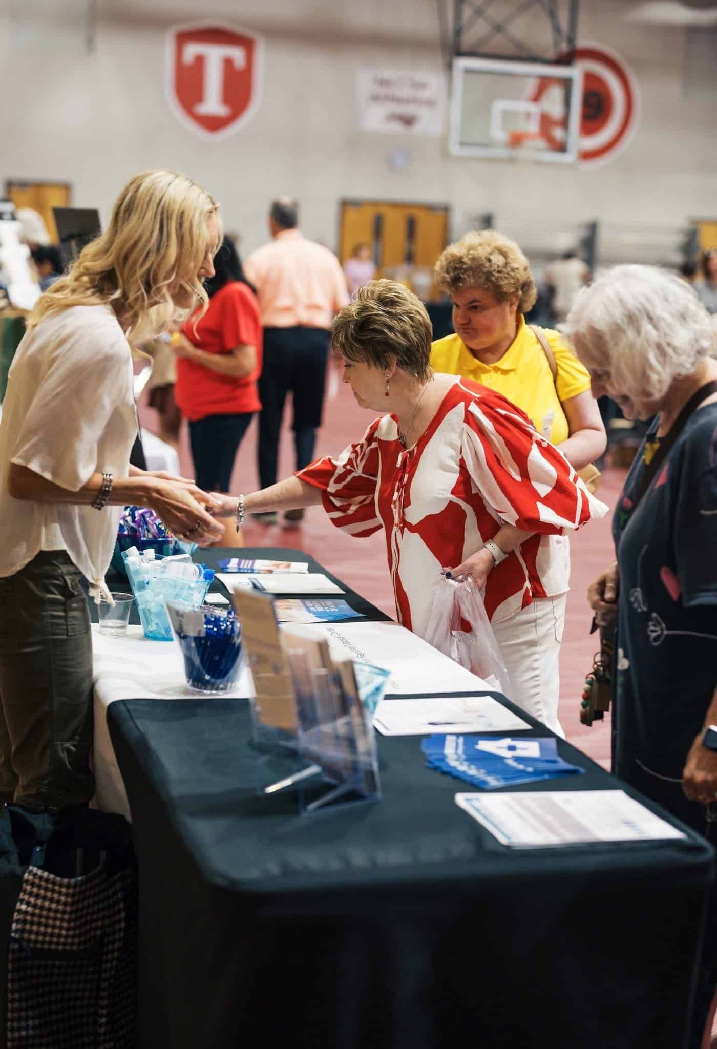 People at a registration table in a gymnasium, with brochures and water bottles displayed