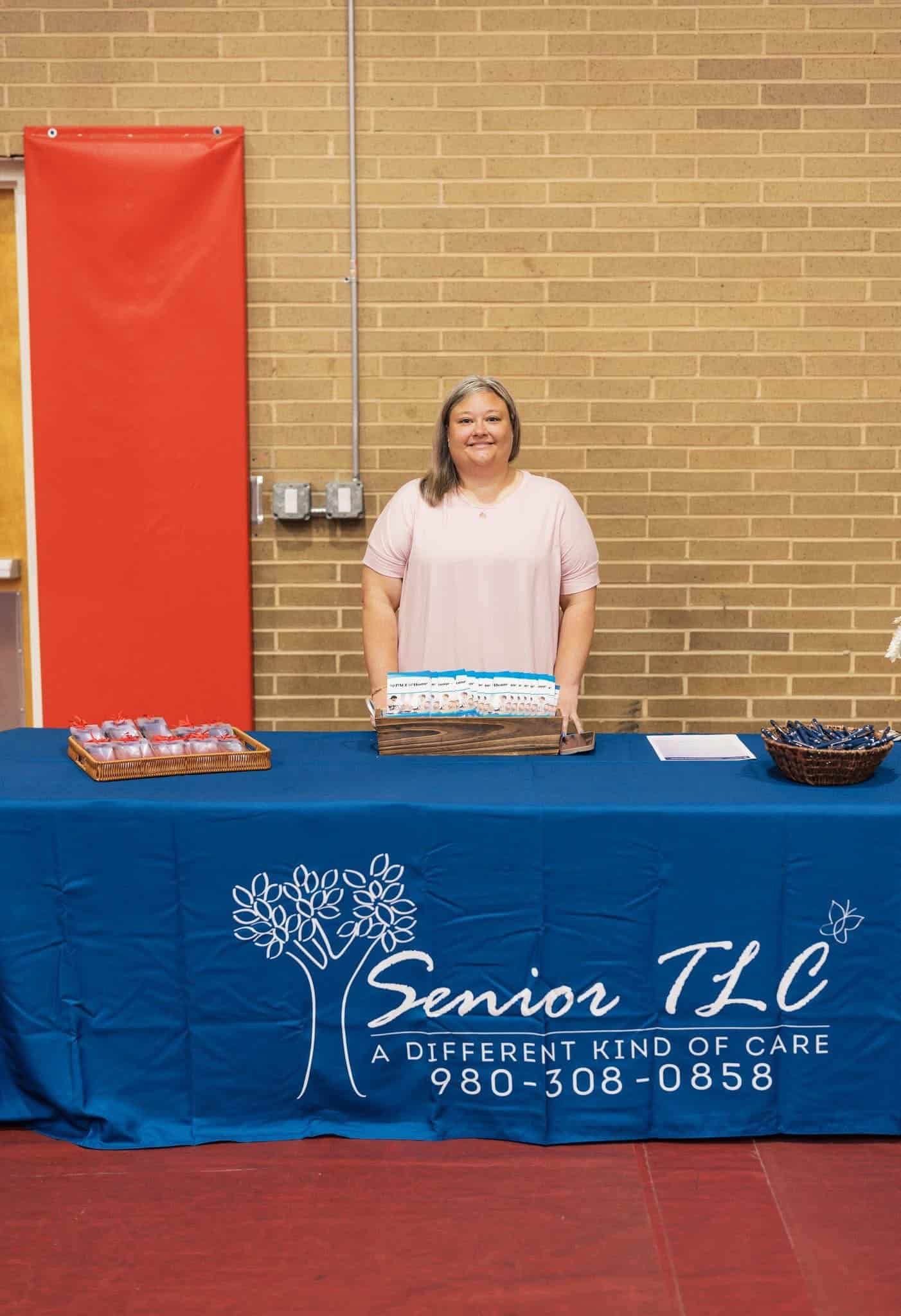 Woman standing behind a table with baked goods at a Senior TLC fundraiser booth.