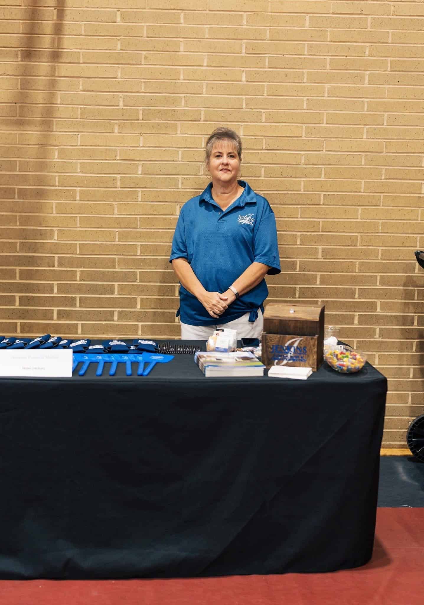 Woman behind a display table with samples and brochures against a brick wall.