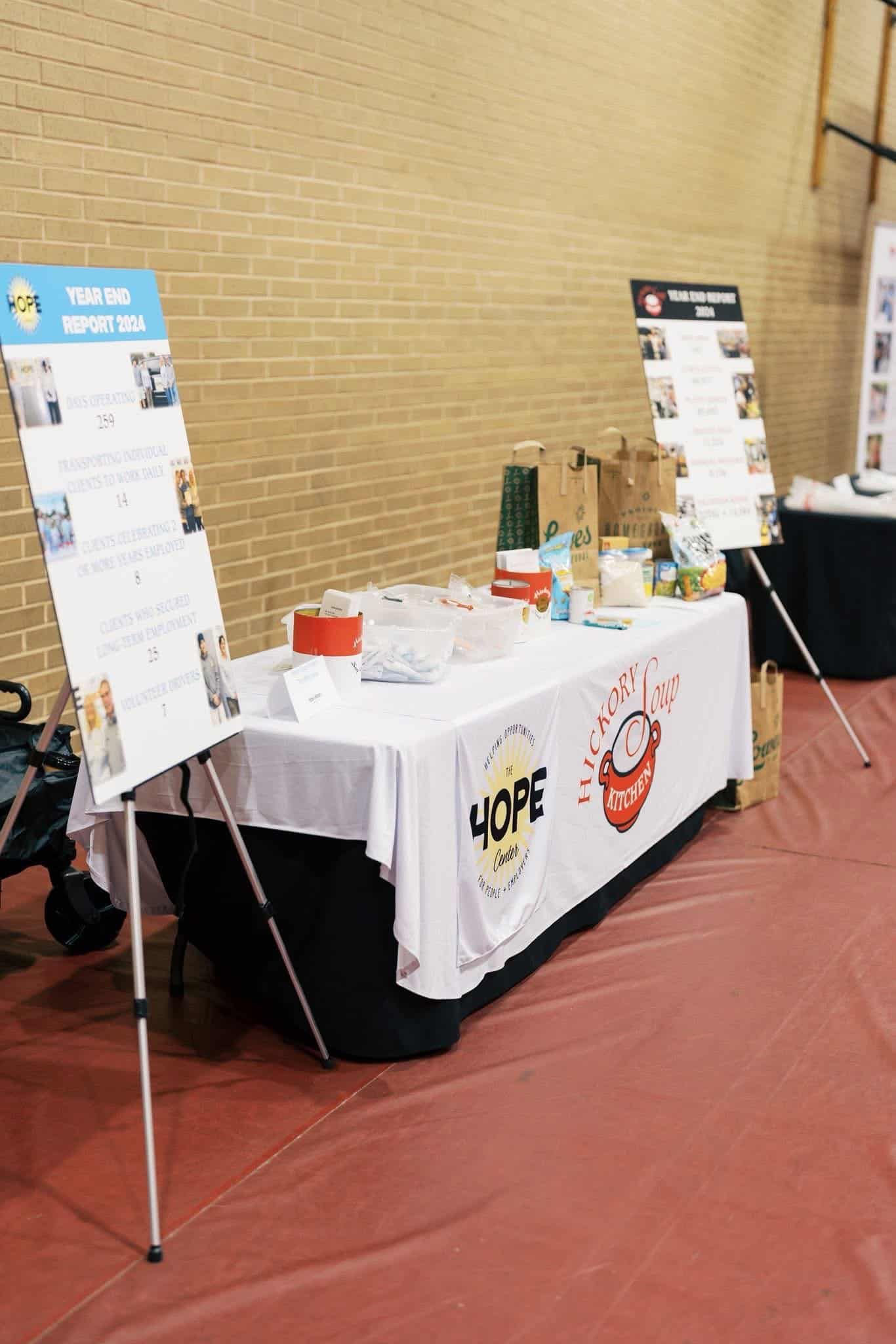 Promotional table with flyers and products at an indoor event, flanked by two poster stands.