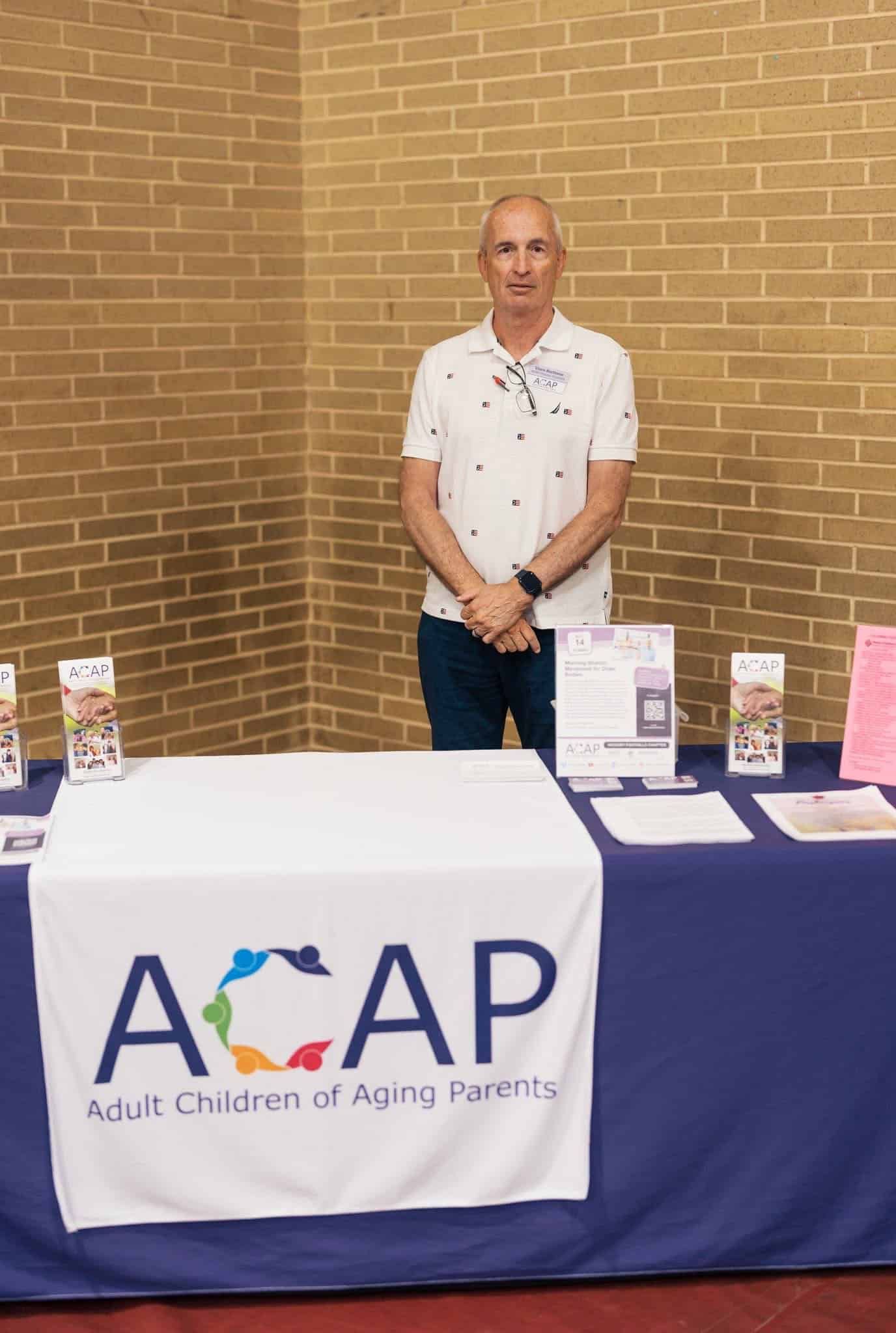 Man standing behind an AOAP event table with brochures and signs against a brick wall