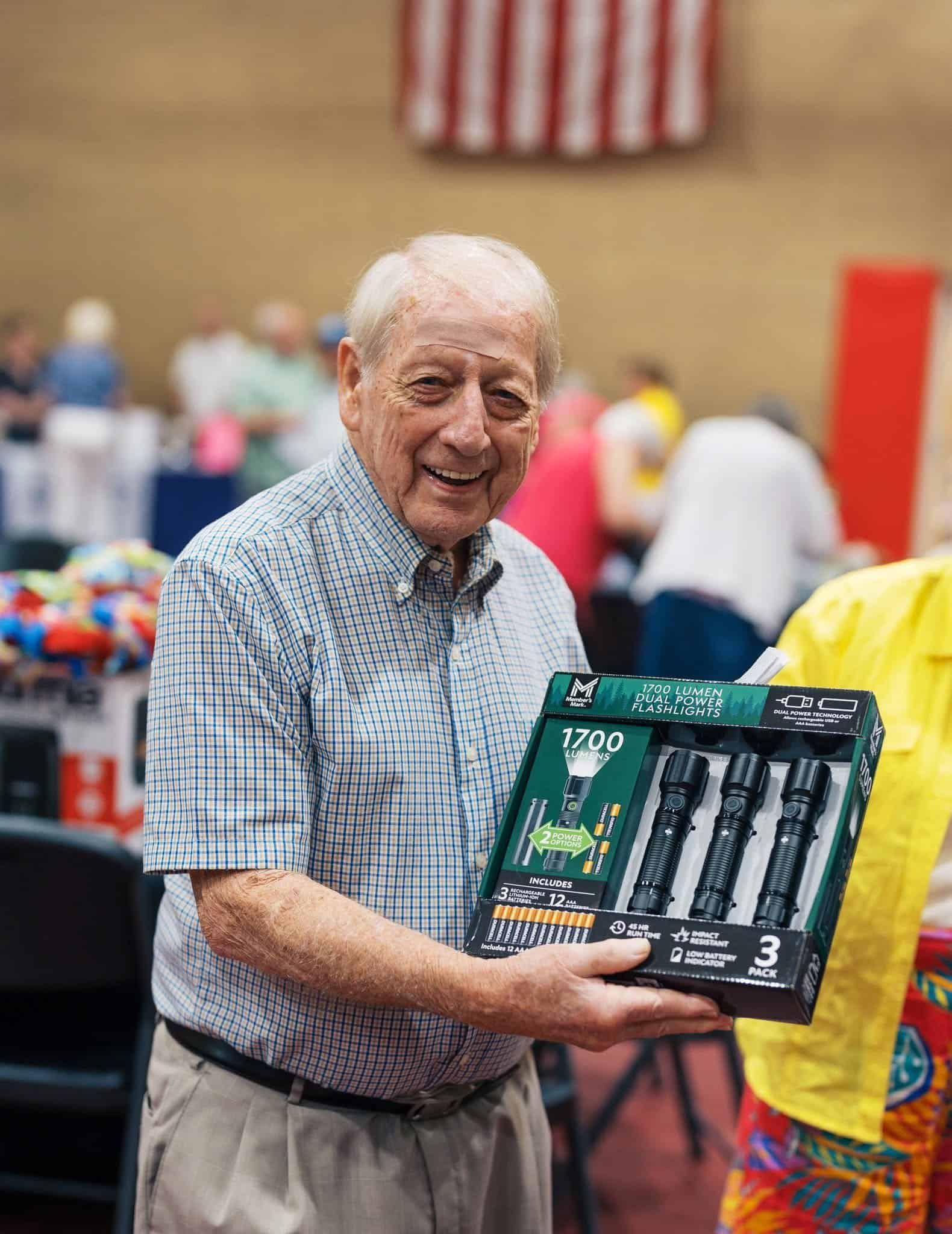 Elderly man smiling and holding a boxed tool set at an indoor event