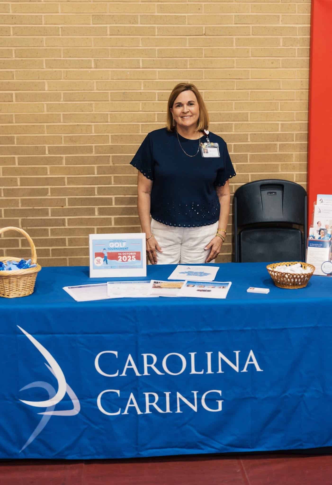 Woman at a Carolina Caring booth with a blue tablecloth and brochures on display.