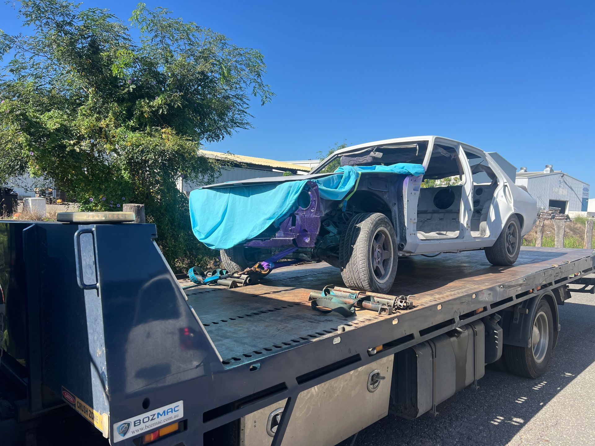 A Blue Tow Truck Is Carrying A White Car — Rockhampton Towing And Transport in Blackwater, QLD