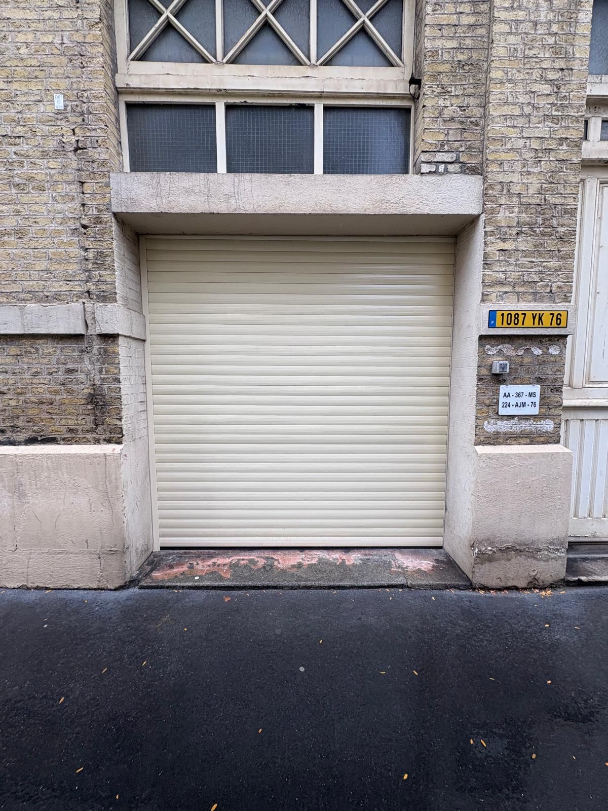 Porte de garage blanche sur une maison beige clair avec un toit gris foncé, une allée en gravier et une petite fenêtre.