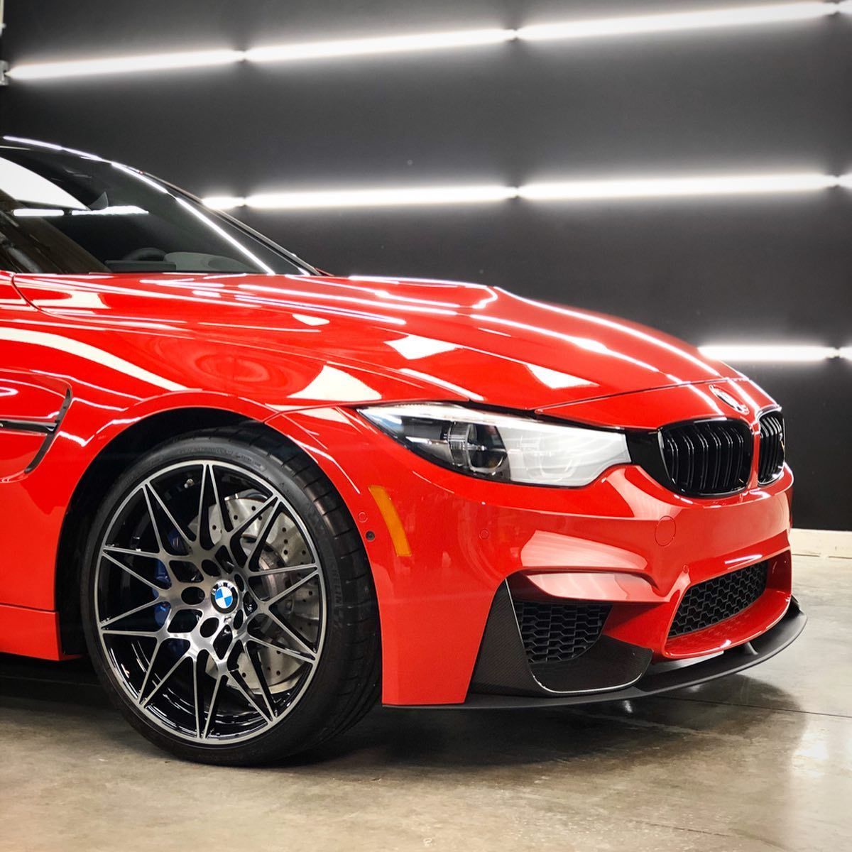 A red bmw is parked in front of a black wall