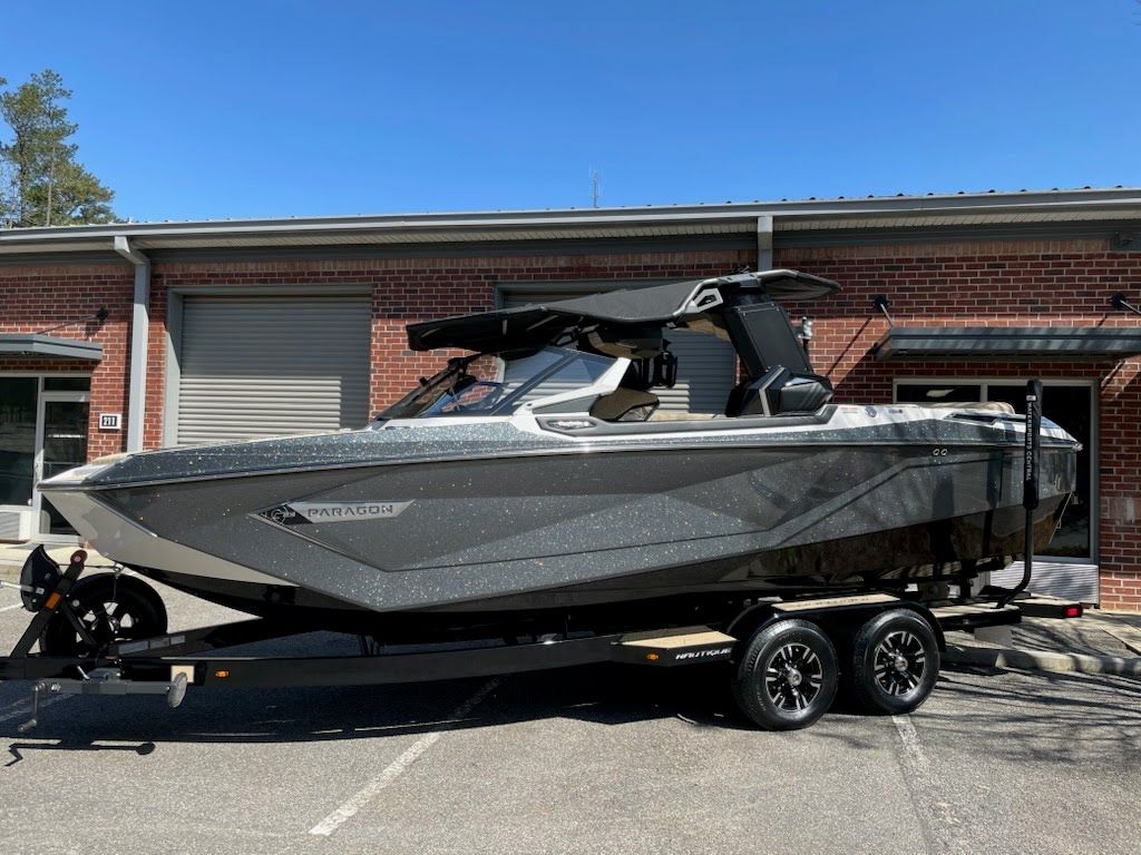 Gray and black boat on a trailer in front of a brick building under a sunny sky.