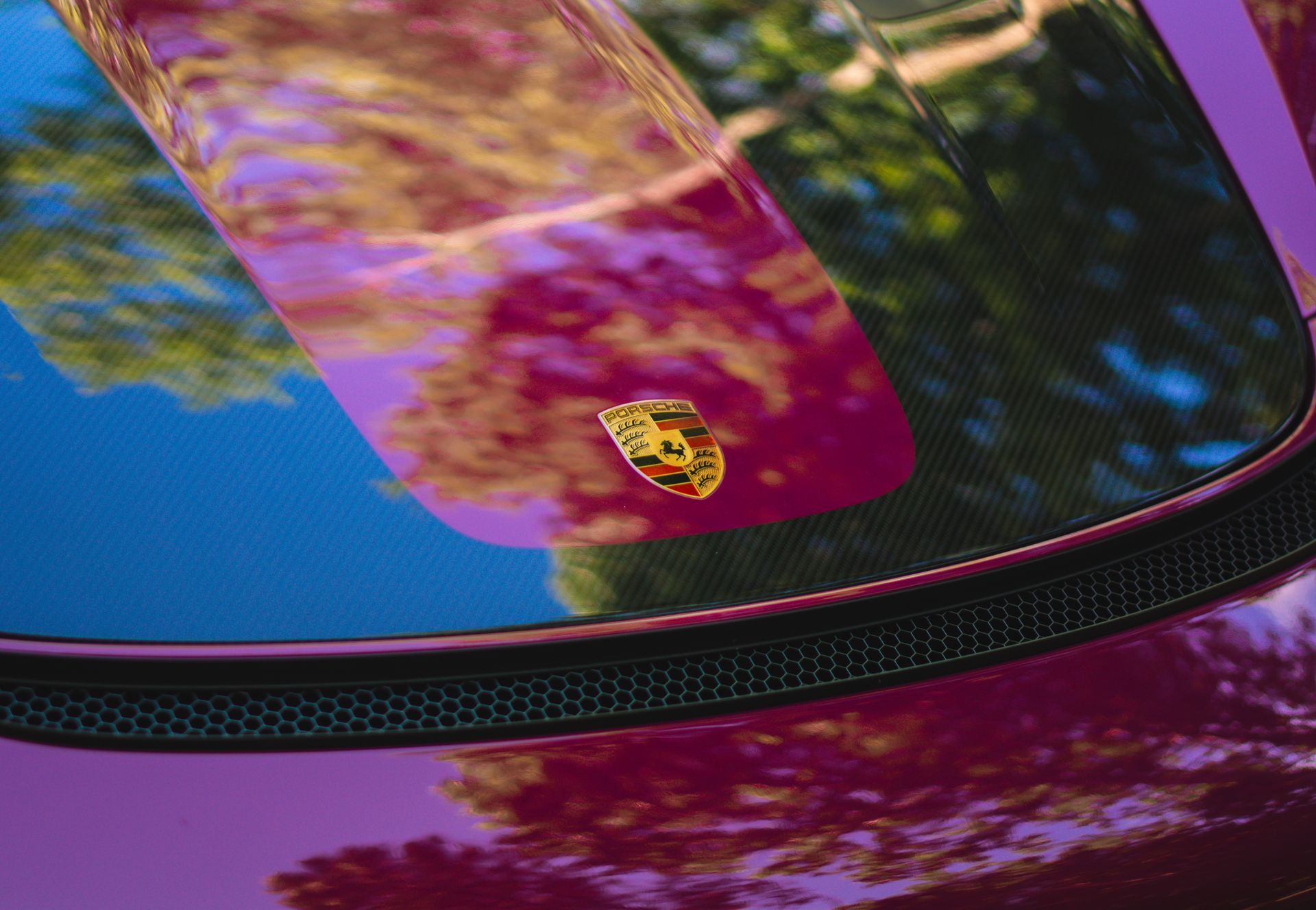 Close-up of a dark purple Porsche with a carbon fiber roof and the Porsche crest.