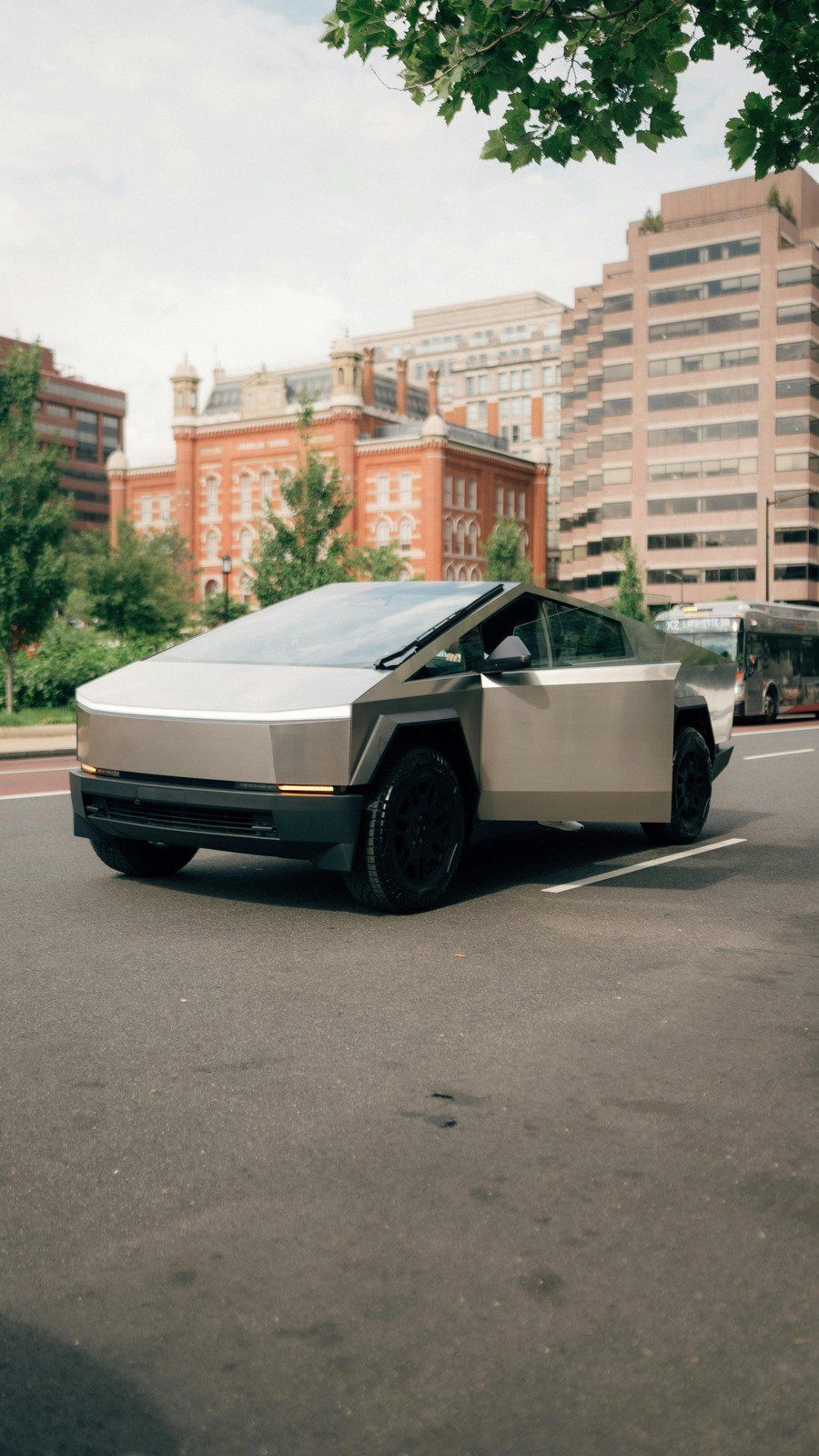 Tesla Cybertruck parked on a city street with apartment buildings and trees in the background