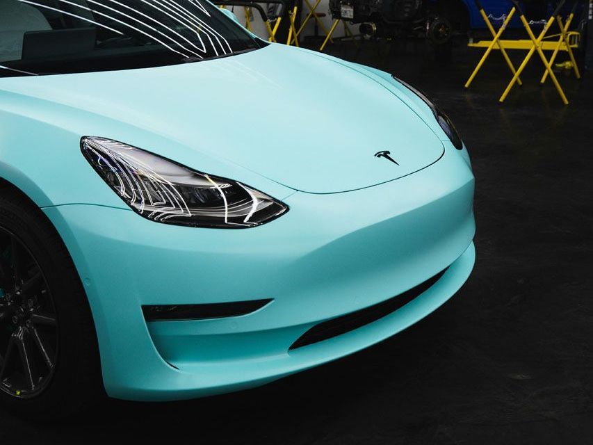 Light blue Tesla car front end parked indoors on a dark floor.
