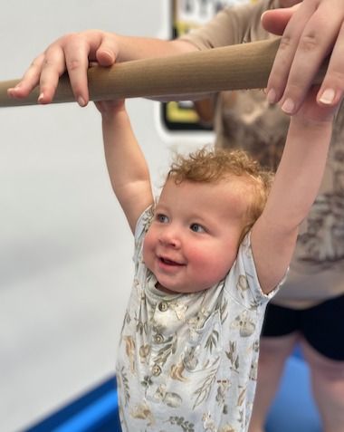 A Baby Is Hanging From A Bar And Smiling — Gold Medal Gymnastics In Molendinar, QLD