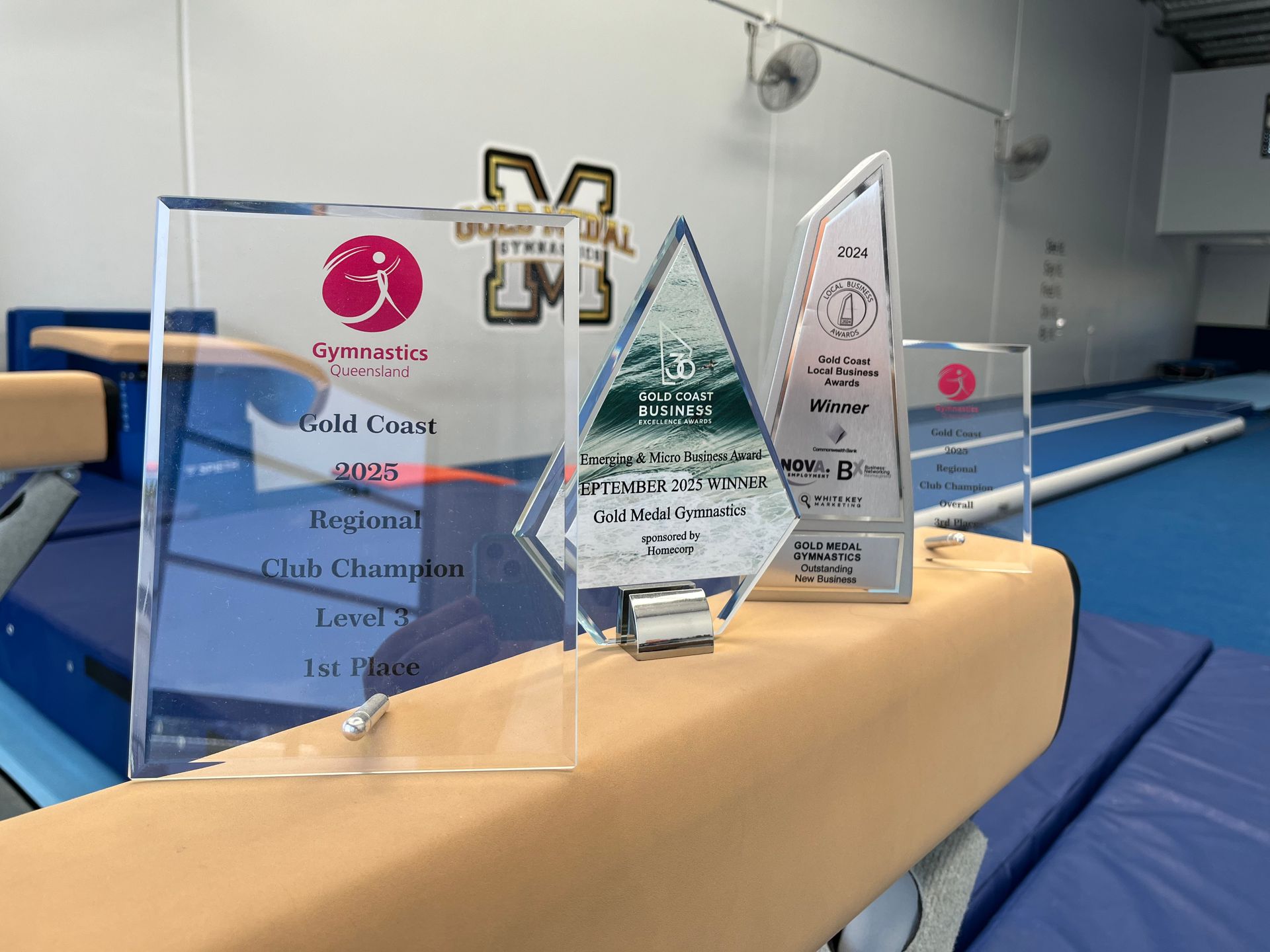 Trophies on balance beam in a gym;  Regional Club Champion Level 7, 1st Place.
