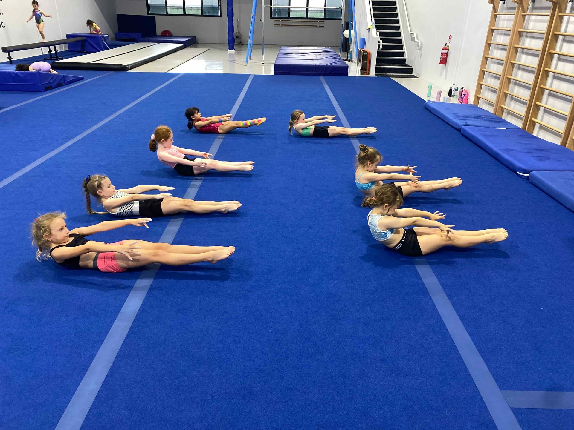 A Group of Young Girls Are Doing Exercises on a Blue Mat in a Gym — Gold Medal Gymnastics In Molendinar, QLD