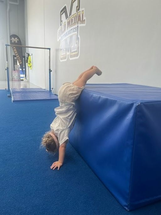 A Little Girl Is Doing A Handstand On A Blue Mat — Gold Medal Gymnastics In Molendinar, QLD