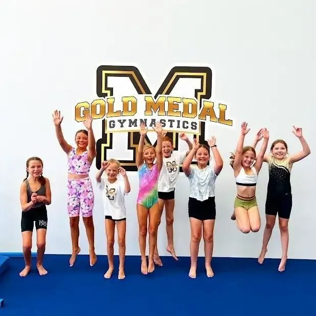 Young Girls Are Jumping In The Air In Front Of A Gold Medal Gymnastics Logo — Gold Medal Gymnastics In Molendinar, QLD