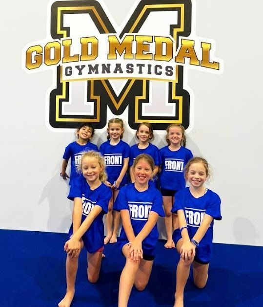 A Group Of Young Girls Are Posing In Front Of A Gold Medal Gymnastics Logo  — Gold Medal Gymnastics In Molendinar, QLD